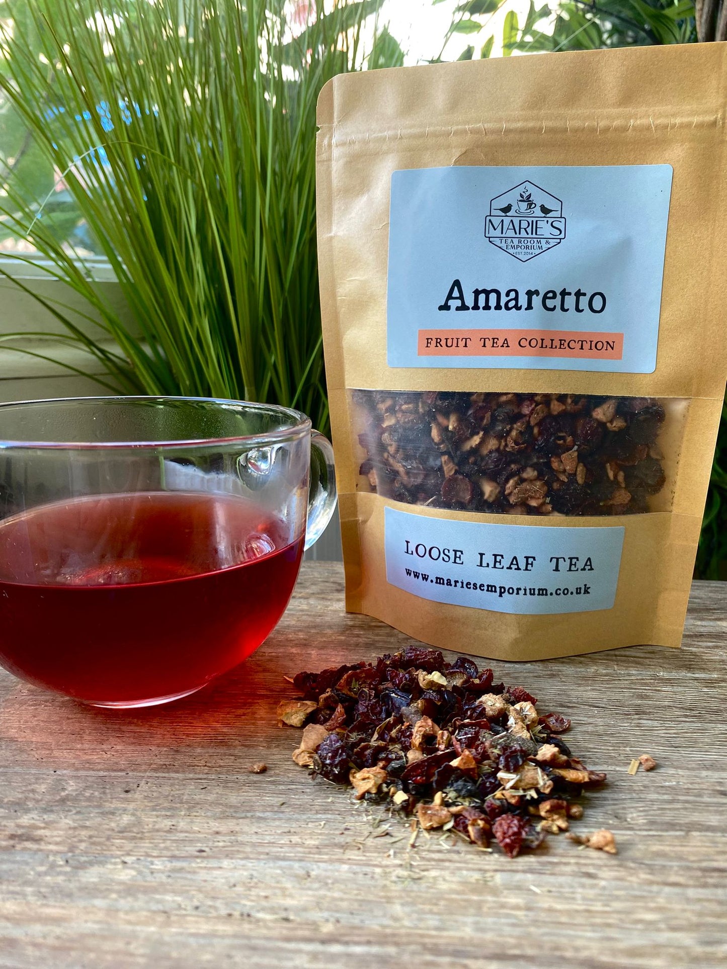 Marie’s Amaretto loose leaf tea package with a cup of brewed tea and loose leaves on a wooden surface.