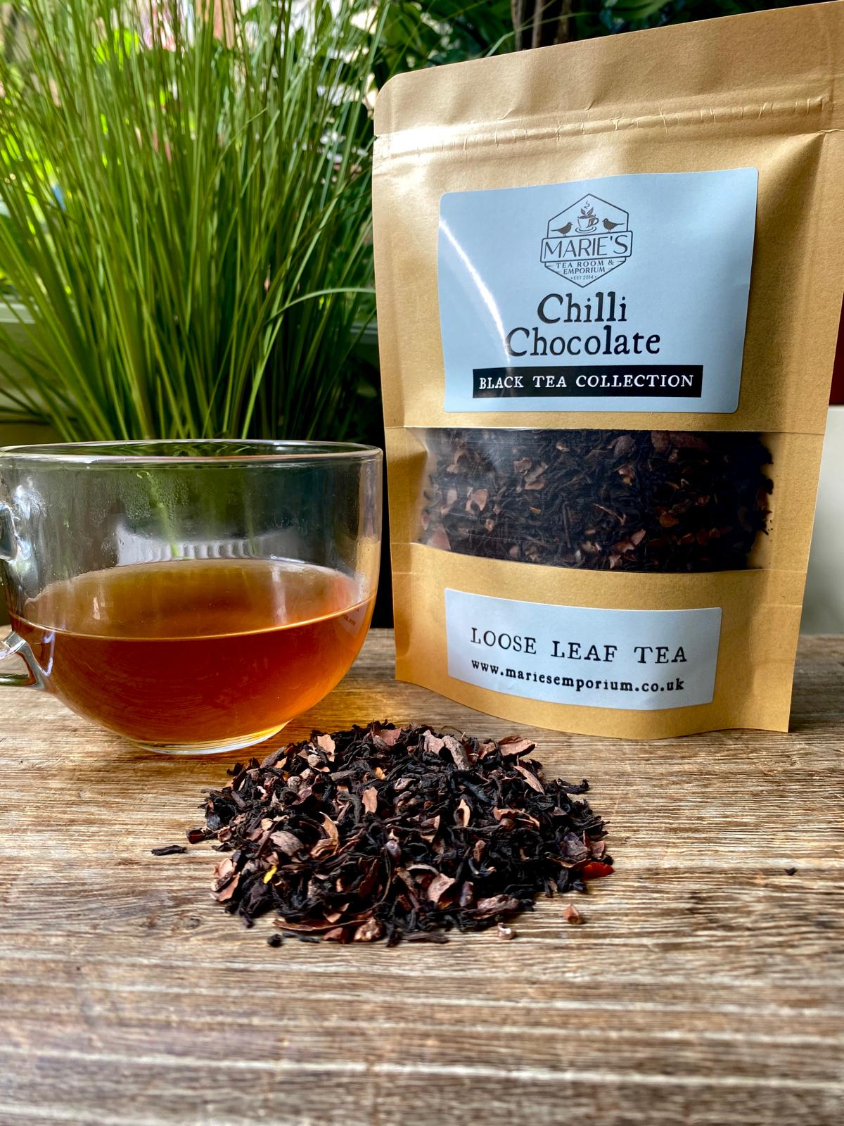 Chilli chocolate black tea package with loose leaf tea and a glass of tea on a wooden surface.