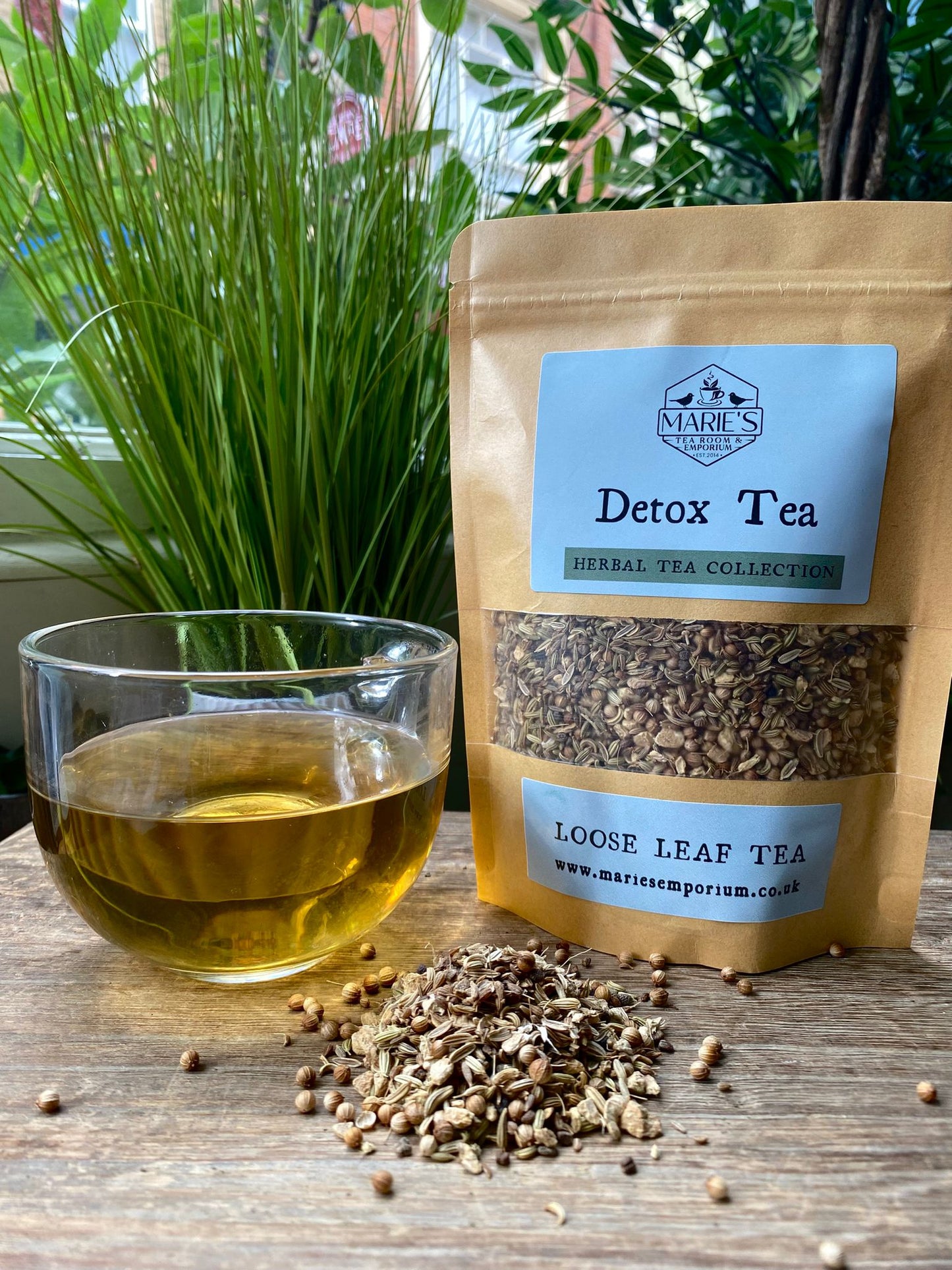 Detox tea packaging with a glass of tea and loose leaves on a wooden surface.