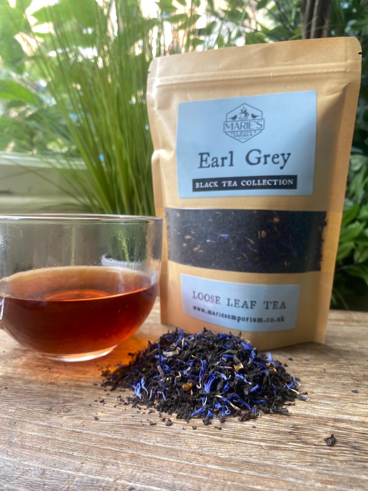 Earl Grey loose leaf tea package with a cup of tea and tea leaves on a wooden surface.