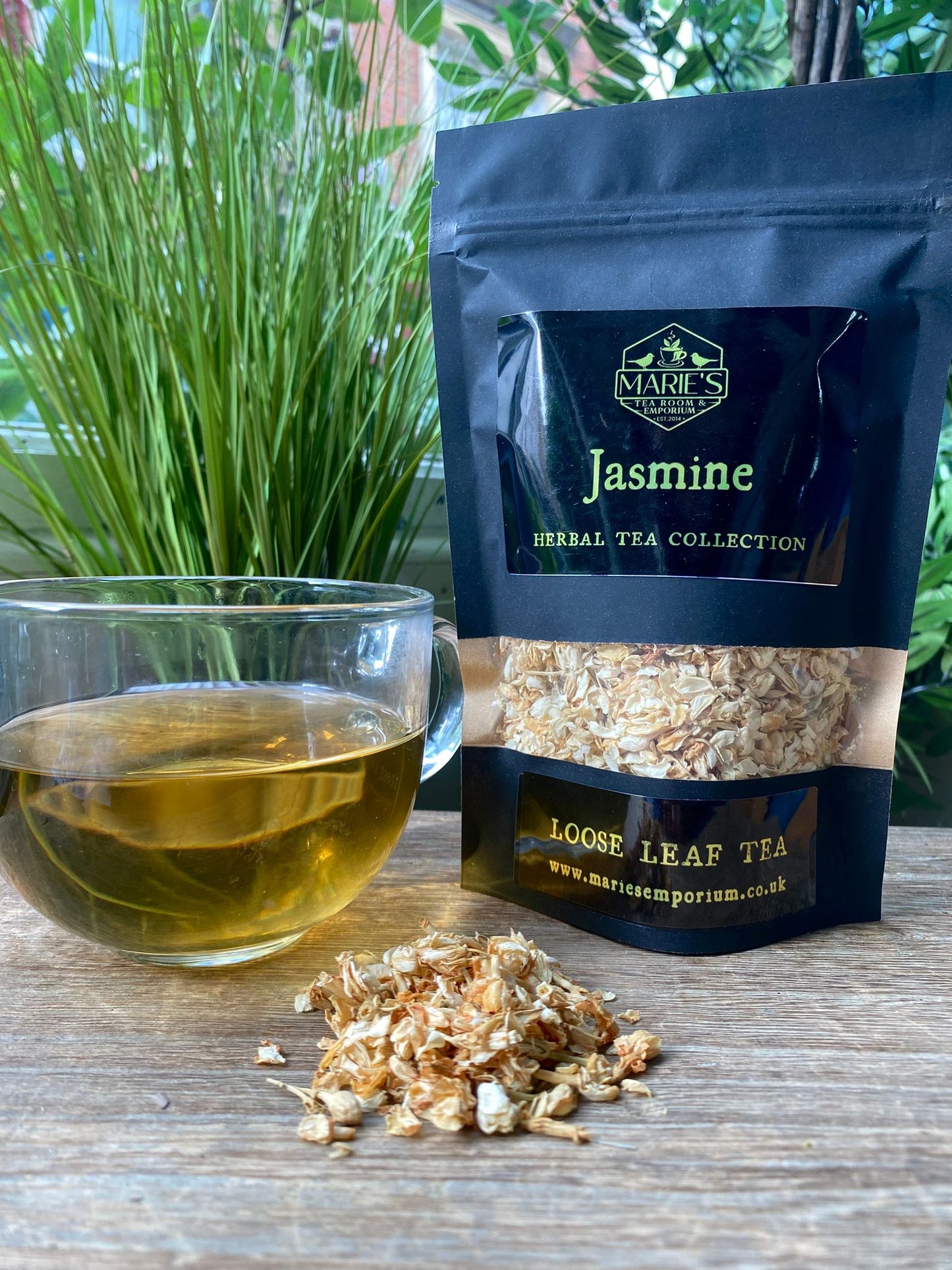 Marie's Emporium Jasmine herbal tea collection with a glass of tea and loose leaf tea on a wooden surface.