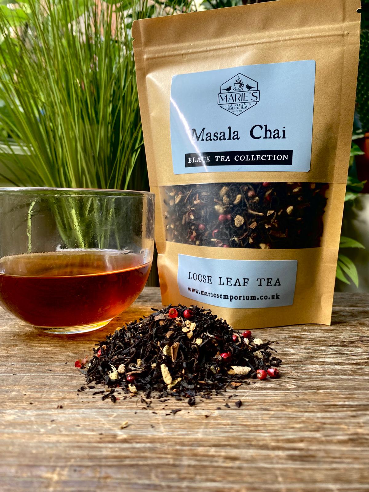 Bag of Marie's Emporium Masala Chai loose leaf tea with a glass of brewed tea on a wooden surface.