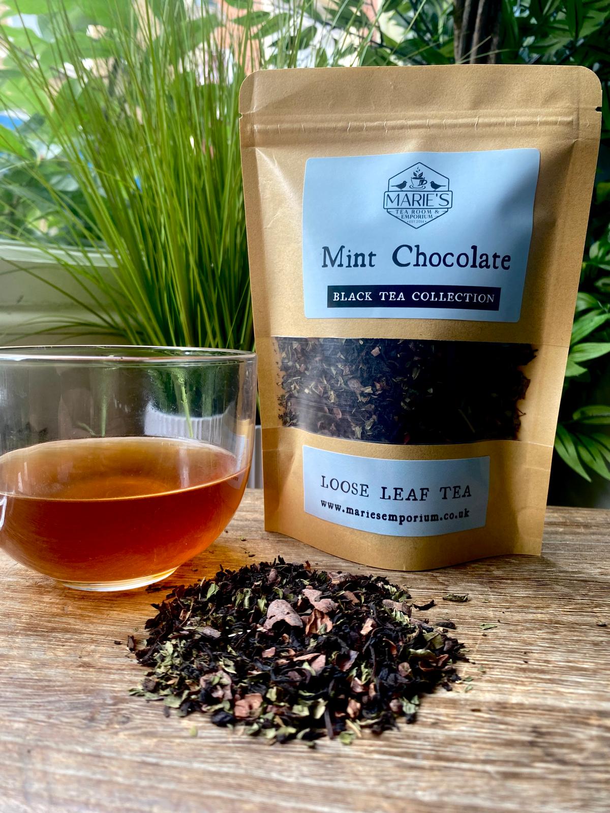 Marie's Emporium Mint Chocolate Black Tea collection with tea leaves and a cup of tea on a wooden surface.