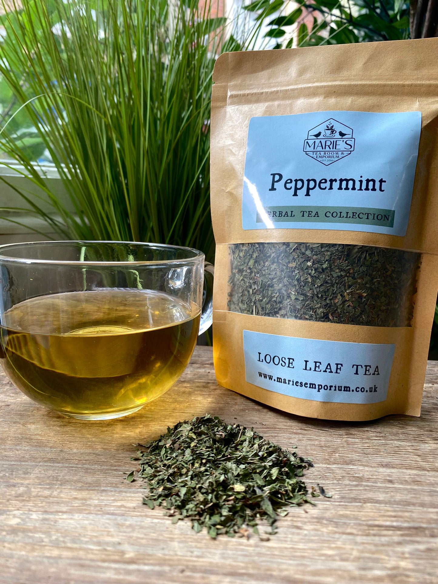 Marie's Emporium peppermint loose leaf tea package with a glass of tea and tea leaves on a wooden surface.