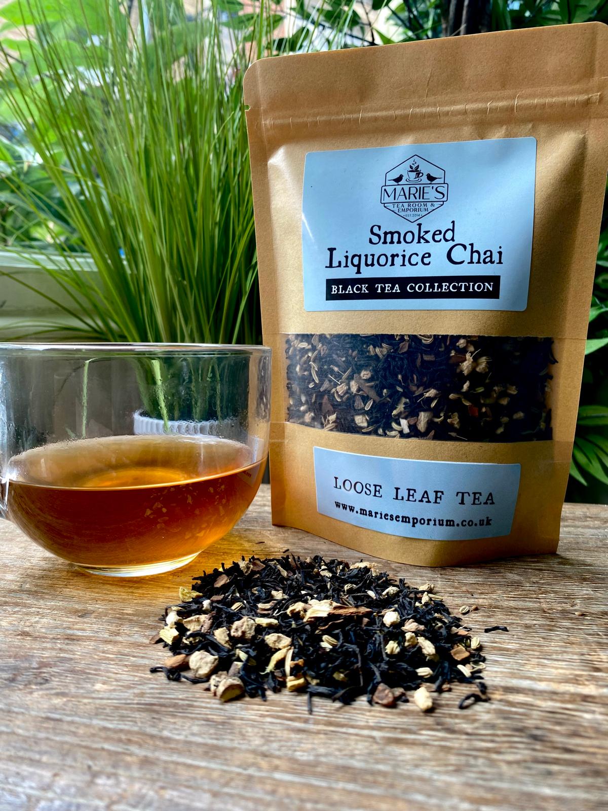 Marie's Emporium Smoked Liquorice Chai loose leaf tea package with a cup of tea and tea leaves on a wooden surface.