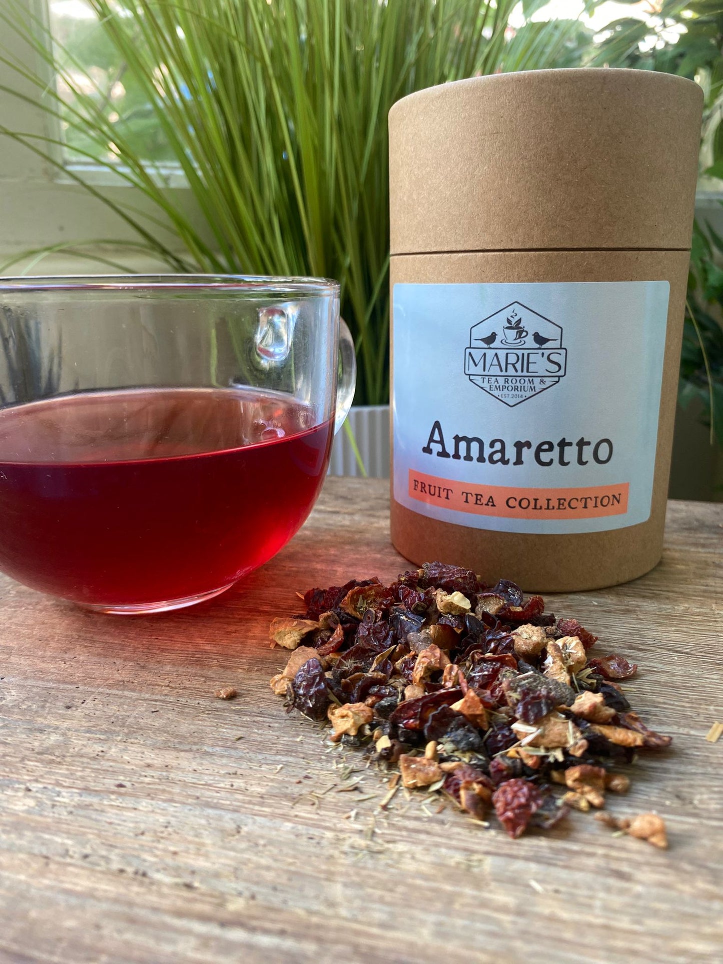 Marie’s Amaretto loose leaf tea packaging with a glass of brewed tea and tea leaves on a wooden surface.