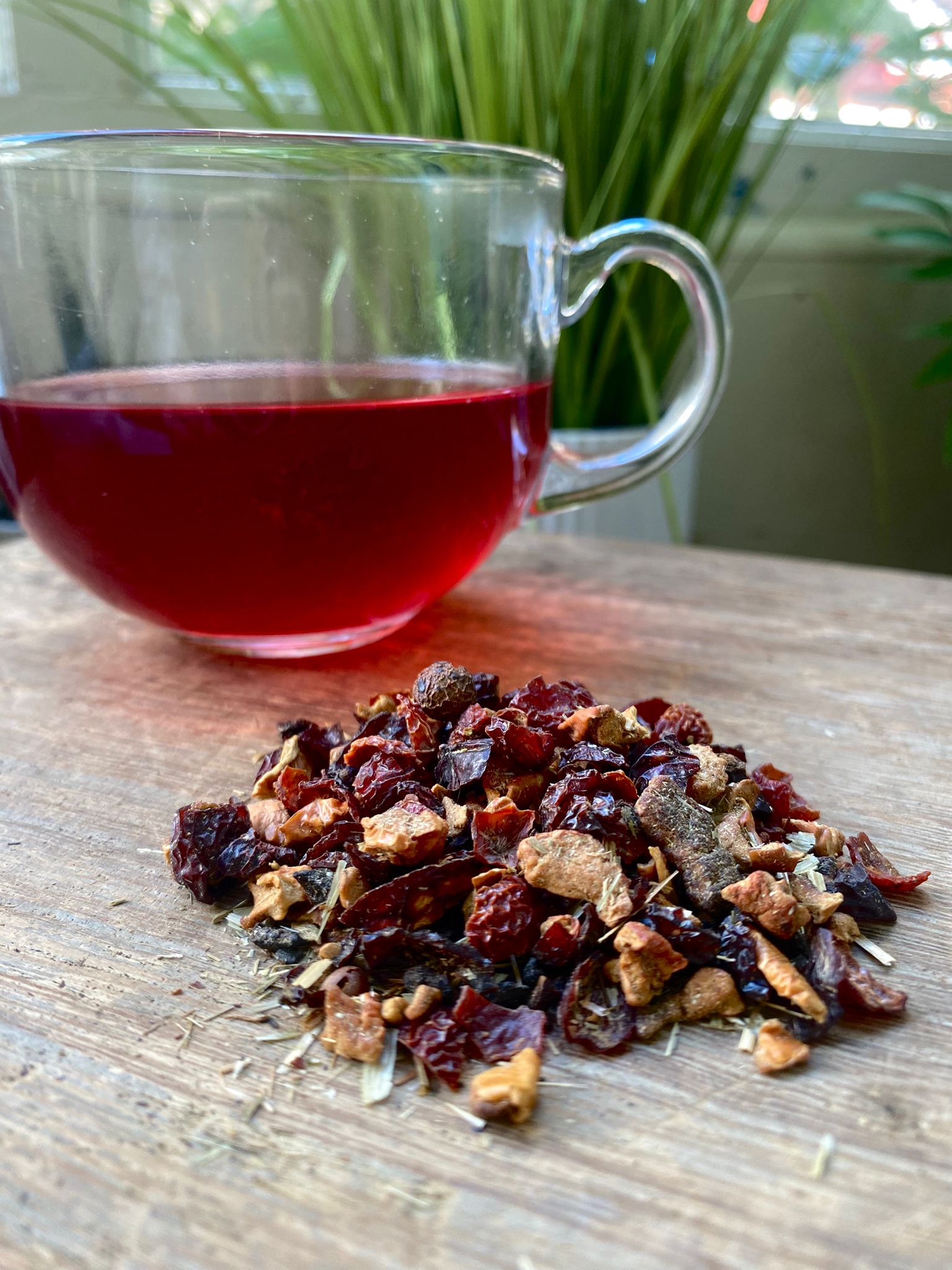Clear glass mug of Marie’s Amaretto loose leaf tea with dried tea leaves on a wooden surface.