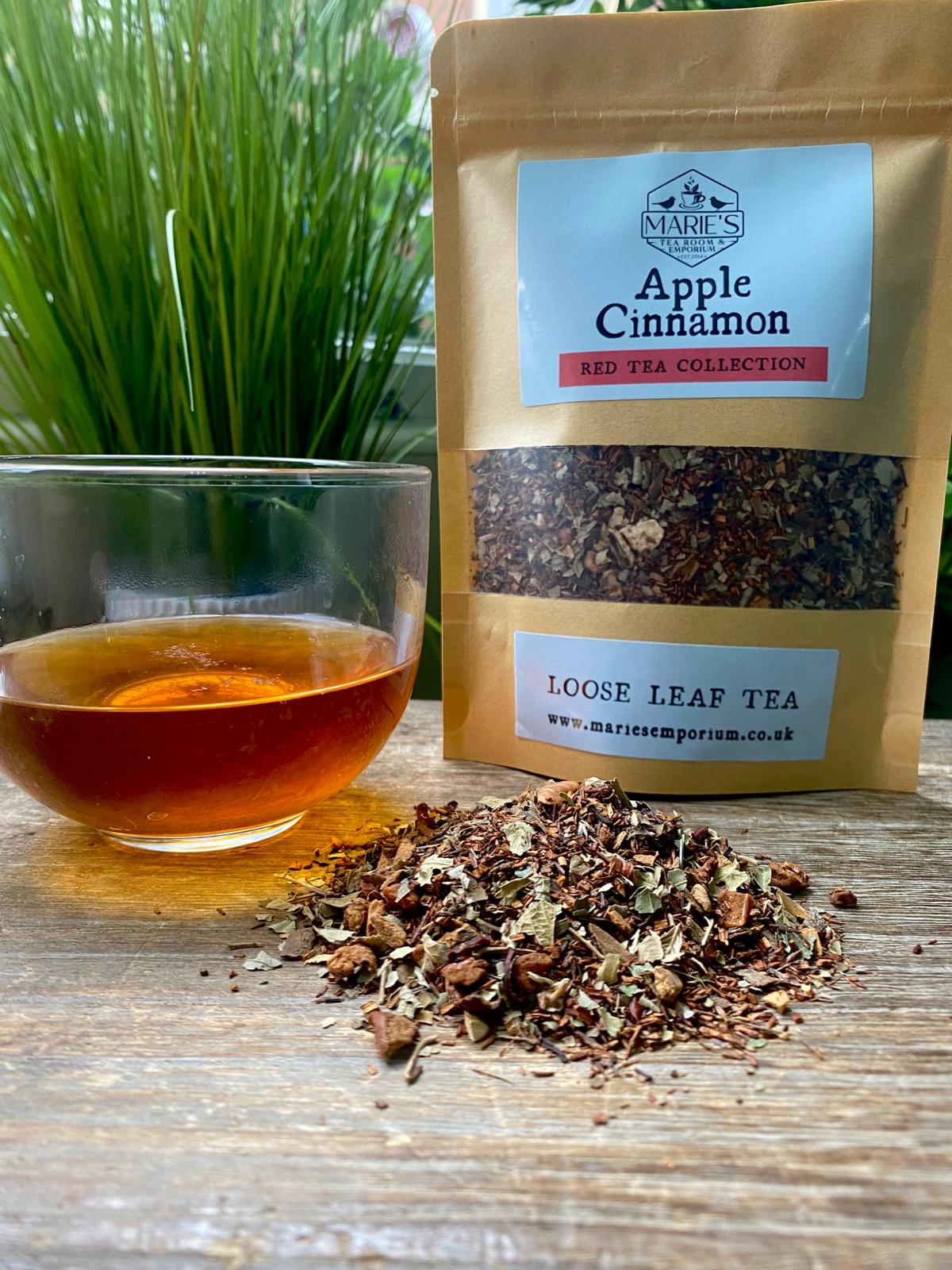 Clear glass cup with amber tea next to a brown paper bag labeled maries Apple Cinnamon Red Tea Collection with Loose tea leaves scattered on a wooden surface.