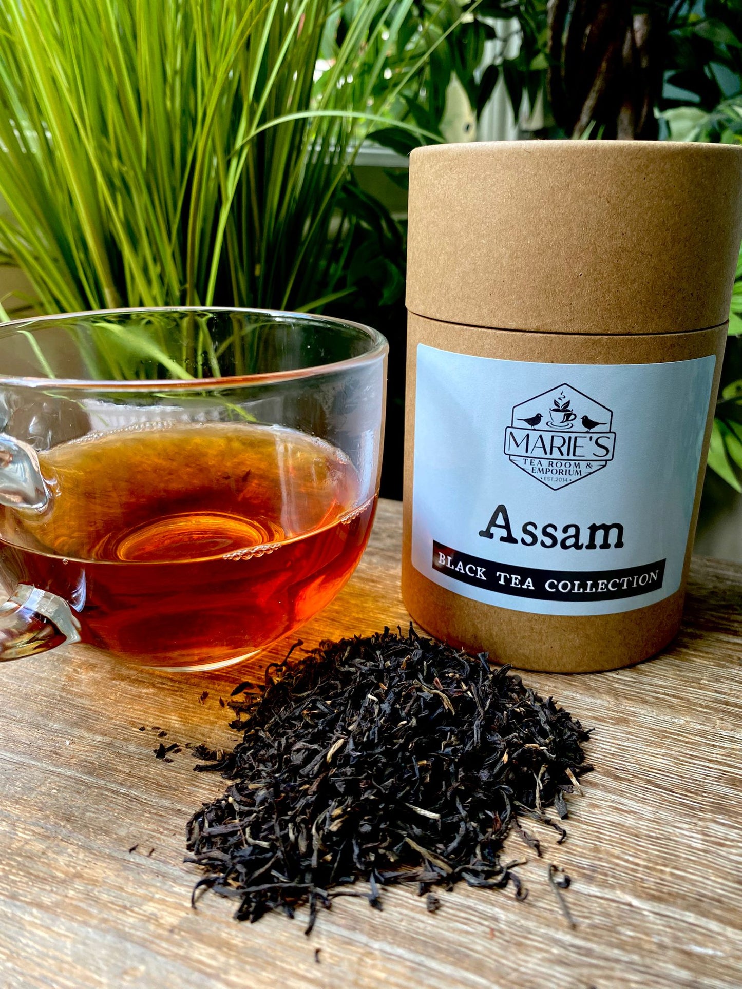 Assam black tea collection with a glass of tea and tea leaves on a wooden surface.