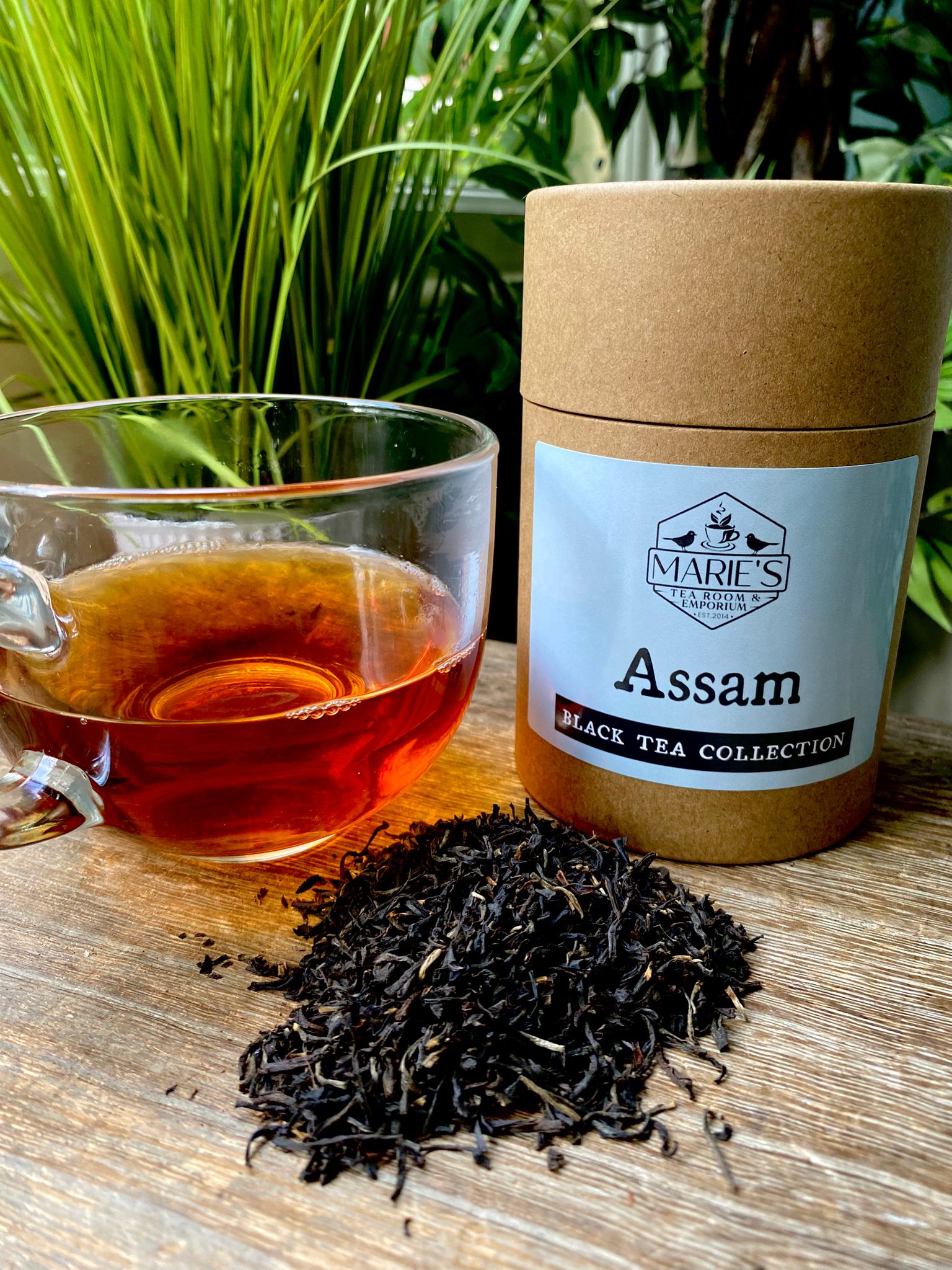 Assam black tea collection with a glass of tea and tea leaves on a wooden surface.