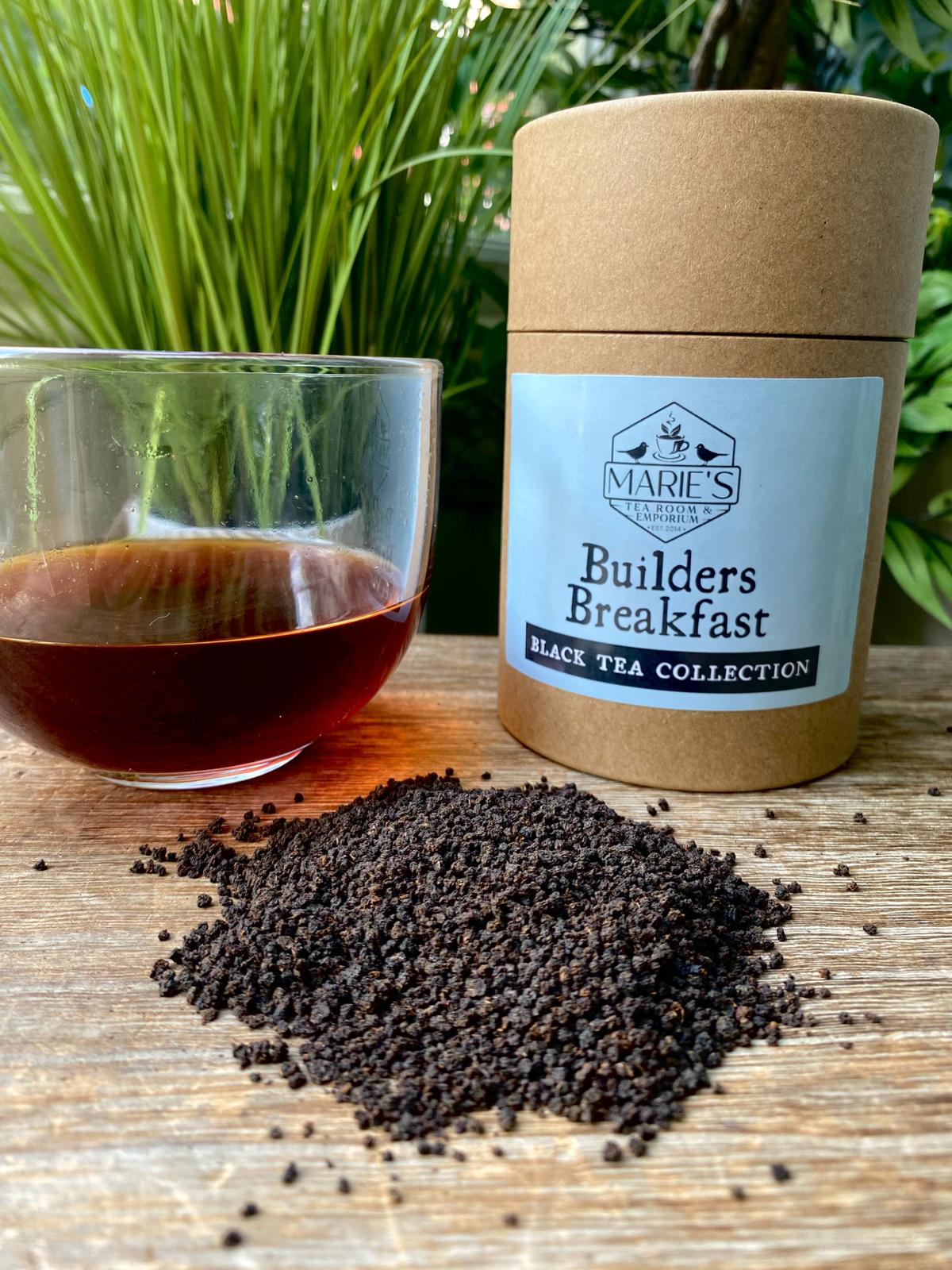 Tea packaging labeled 'Builders Breakfast' from Marie's Tea Collection with loose tea leaves and a glass of tea on a wooden surface.