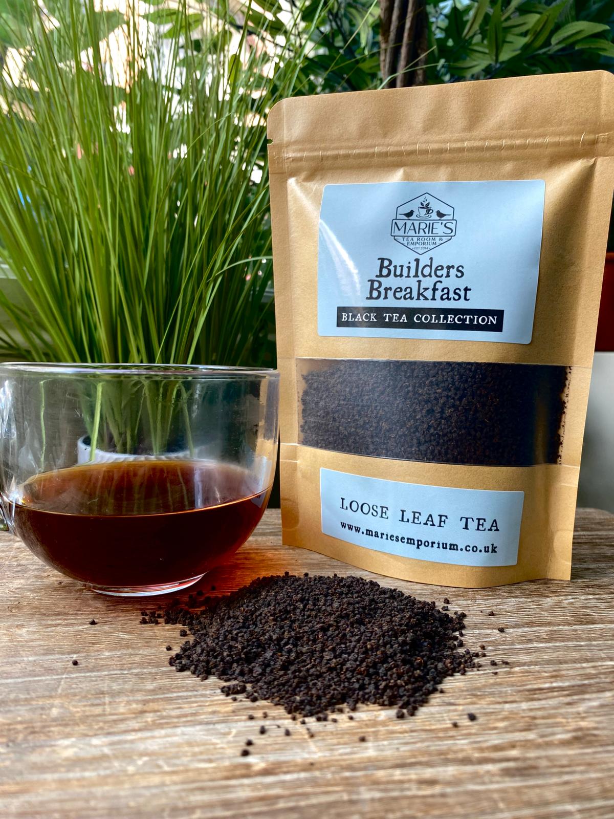 Bag of 'Builders Breakfast' loose leaf tea with a glass of brewed tea on a wooden surface.