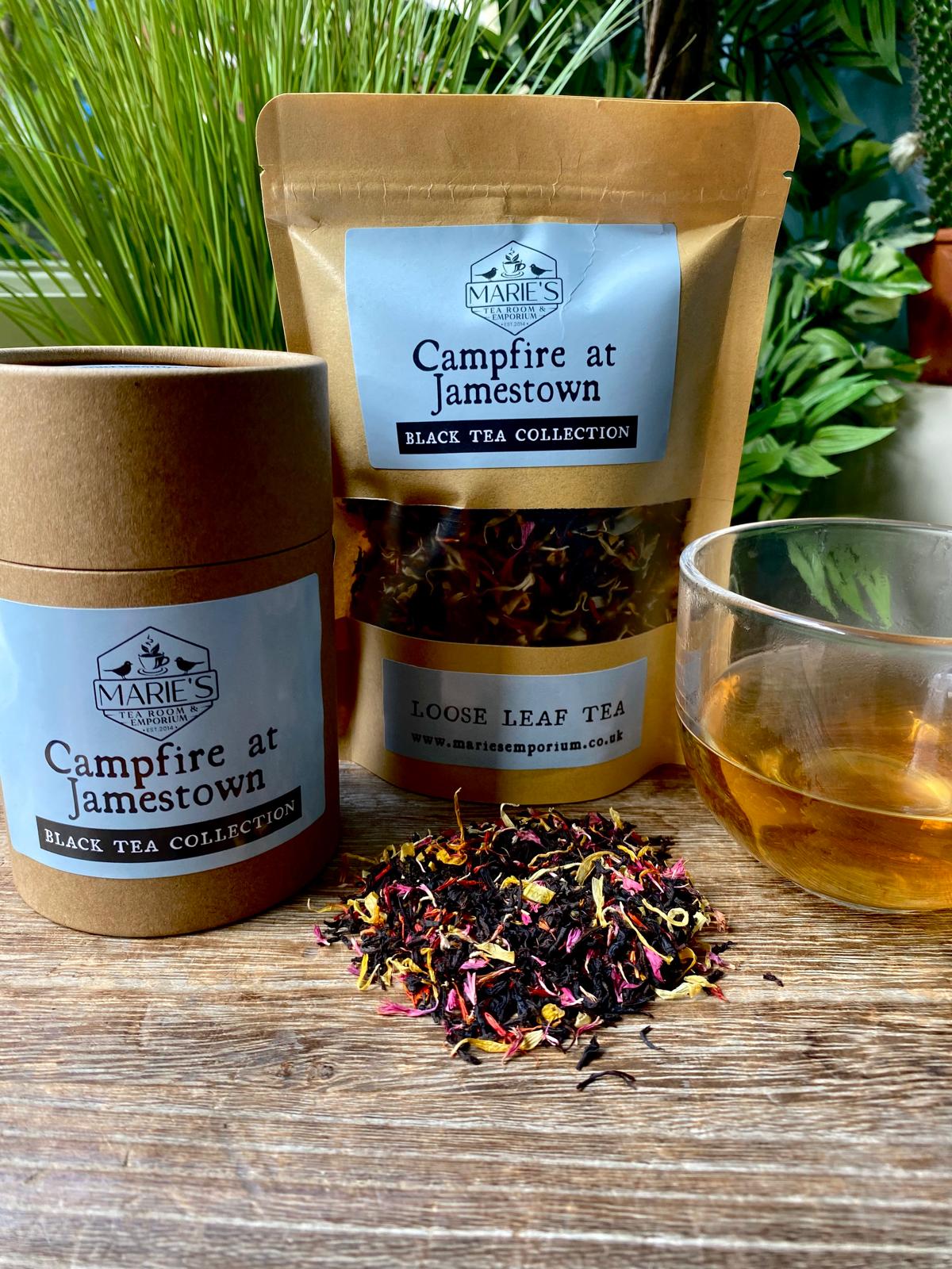 Campfire at Jamestown Tea packaging and loose tea leaves with a glass of tea on a wooden surface.