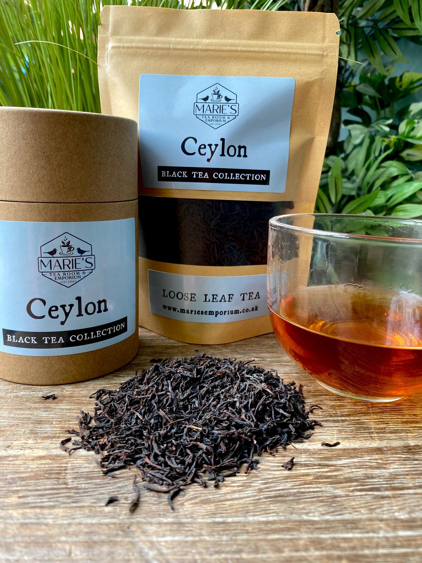 Marie's Emporium Ceylon black tea collection with loose leaf tea, tea leaves, and a glass of tea on a wooden surface.
