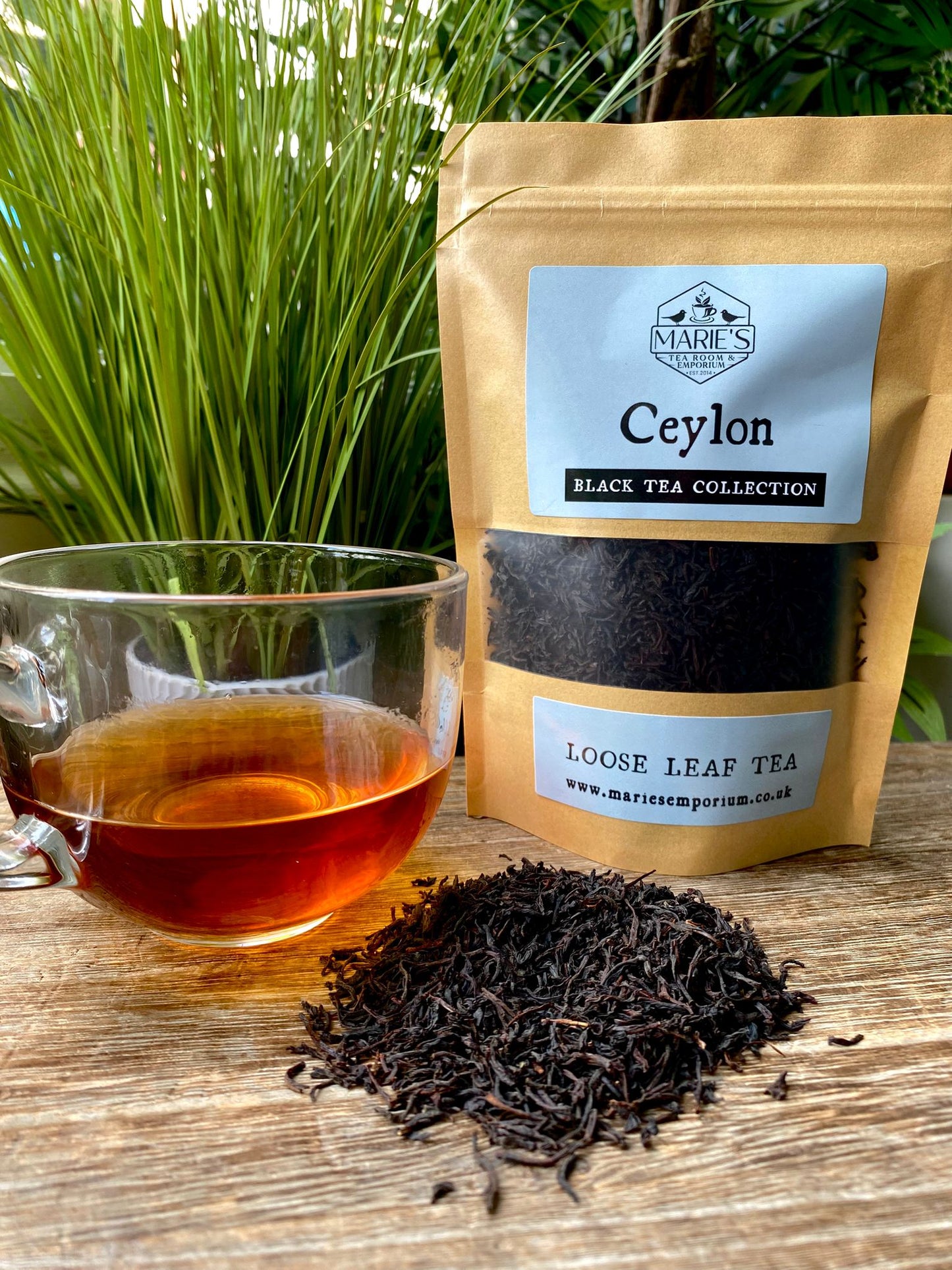 Ceylon black tea package with a cup of tea and loose leaf tea on a wooden surface.