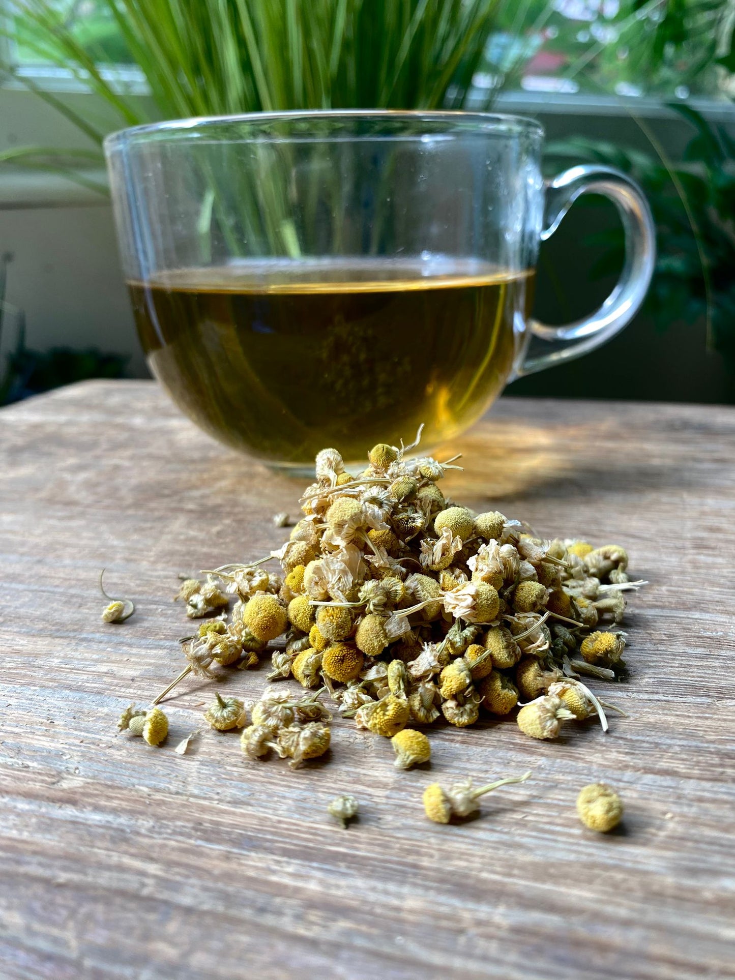 Marie’s chamomile loose leaf tea with brewed herbal tea in a clear glass mug and loose tea leaves on a wooden surface