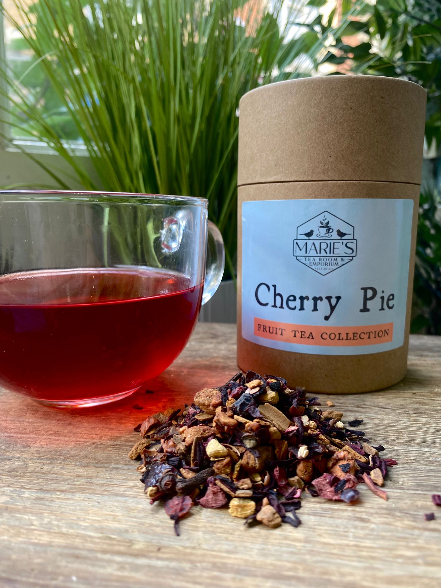 Marie's Tea Collection Cherry Pie fruit tea with a glass of tea and loose teaf tea on a wooden surface.