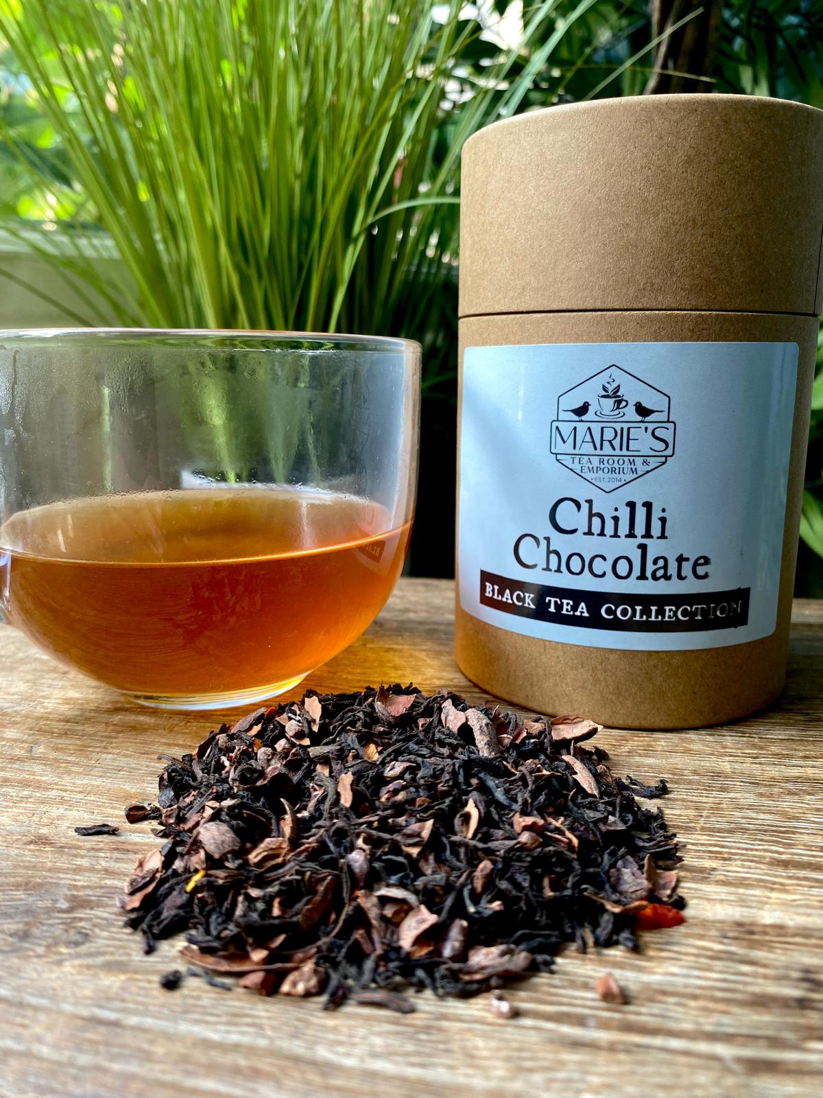 Chilli Chocolate black tea collection with tea leaves and a glass of tea on a wooden surface.