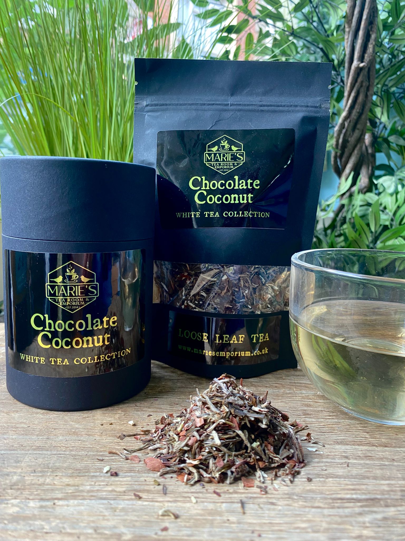 loose leaf chocolate coconut maries Tea packaging and loose tea leaves with a glass of tea on a wooden surface.