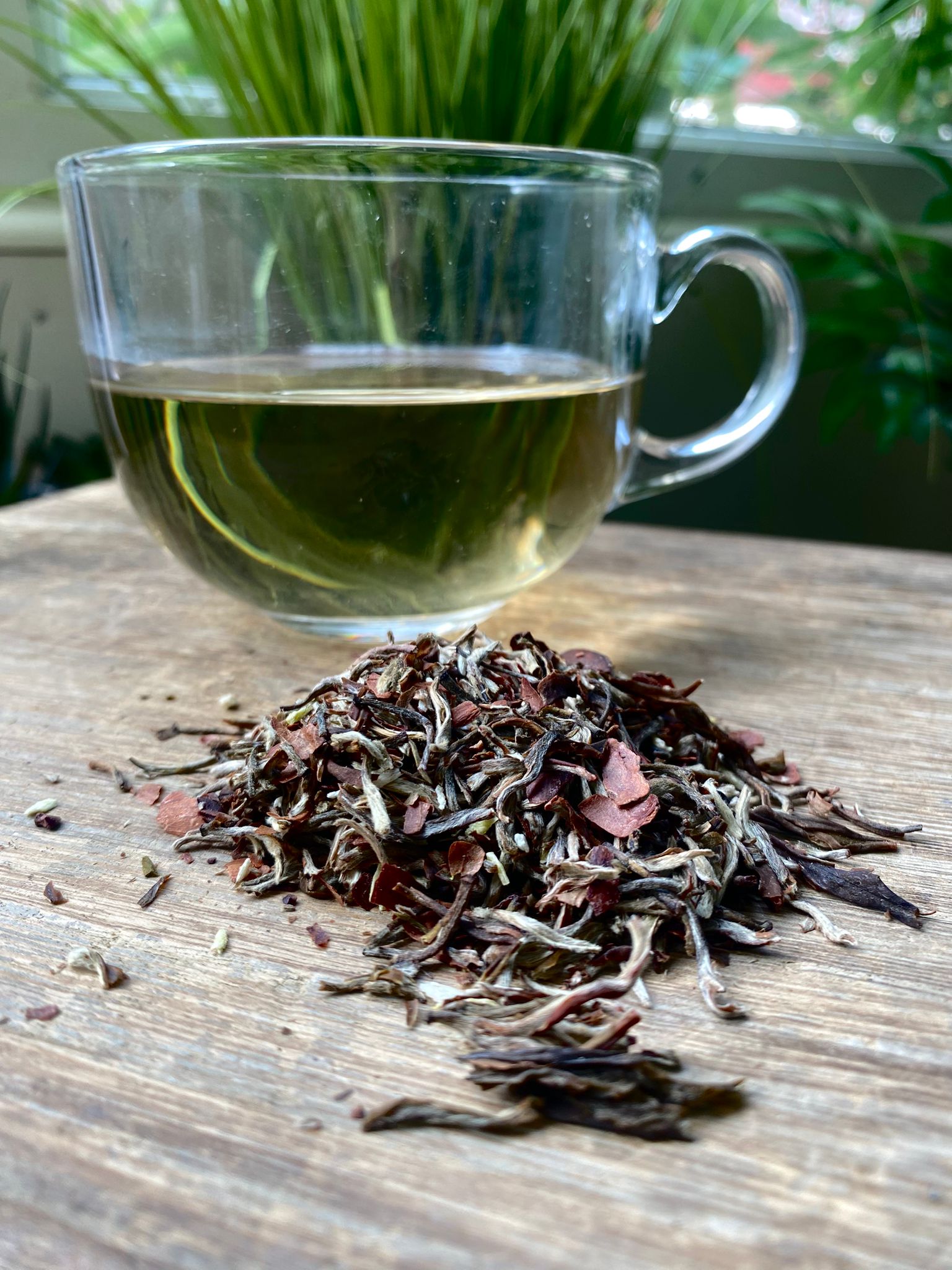 Clear glass mug with maries chocolate coconut loose leaf white tea dried tea leaves on a wooden surface