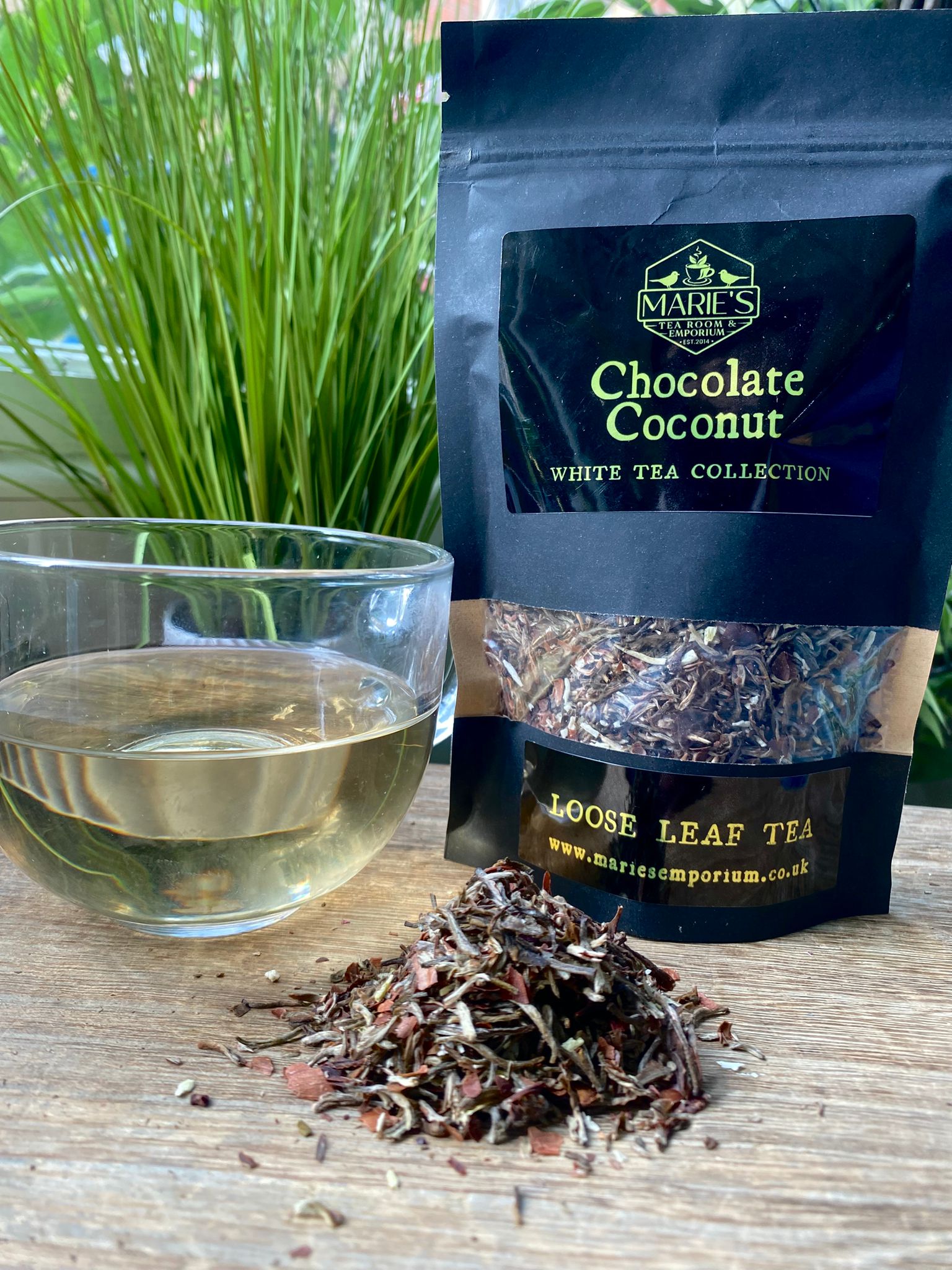 Marie's Chocolate Coconut White Tea package with a glass of tea and loose tea leaves on a wooden surface.
