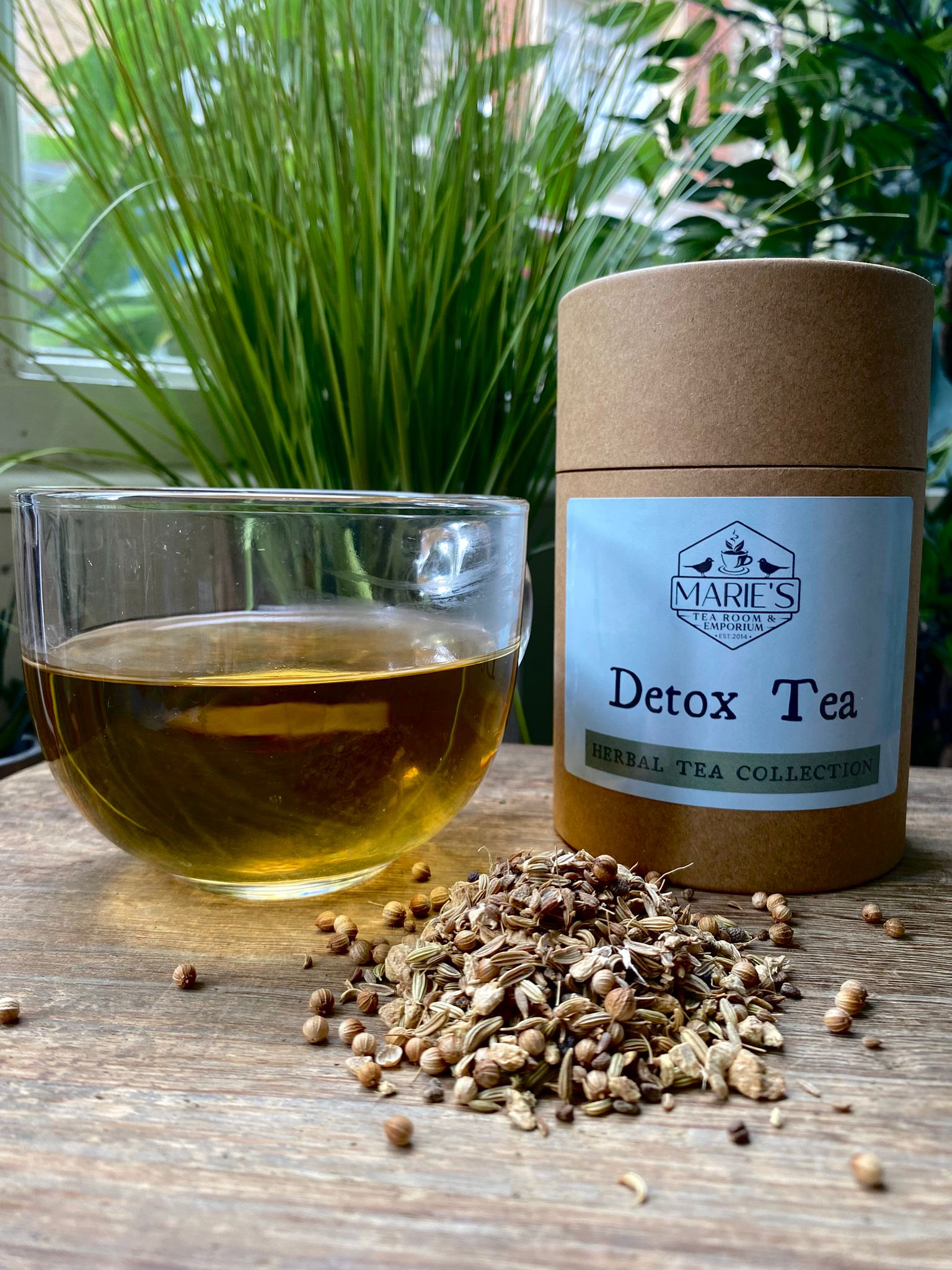 Detox tea with a glass of tea and tea leaves on a wooden surface, branded as Marie's Tea Collection.