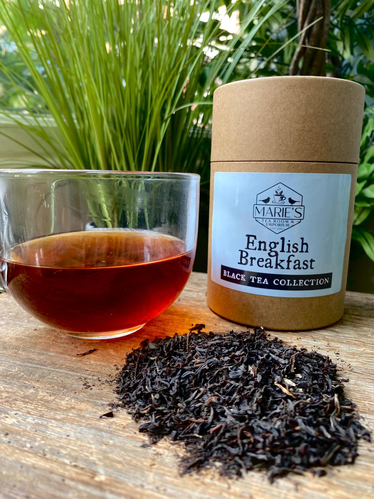 Marie's English Breakfast black tea collection with a glass of tea and loose tea leaves on a wooden surface.
