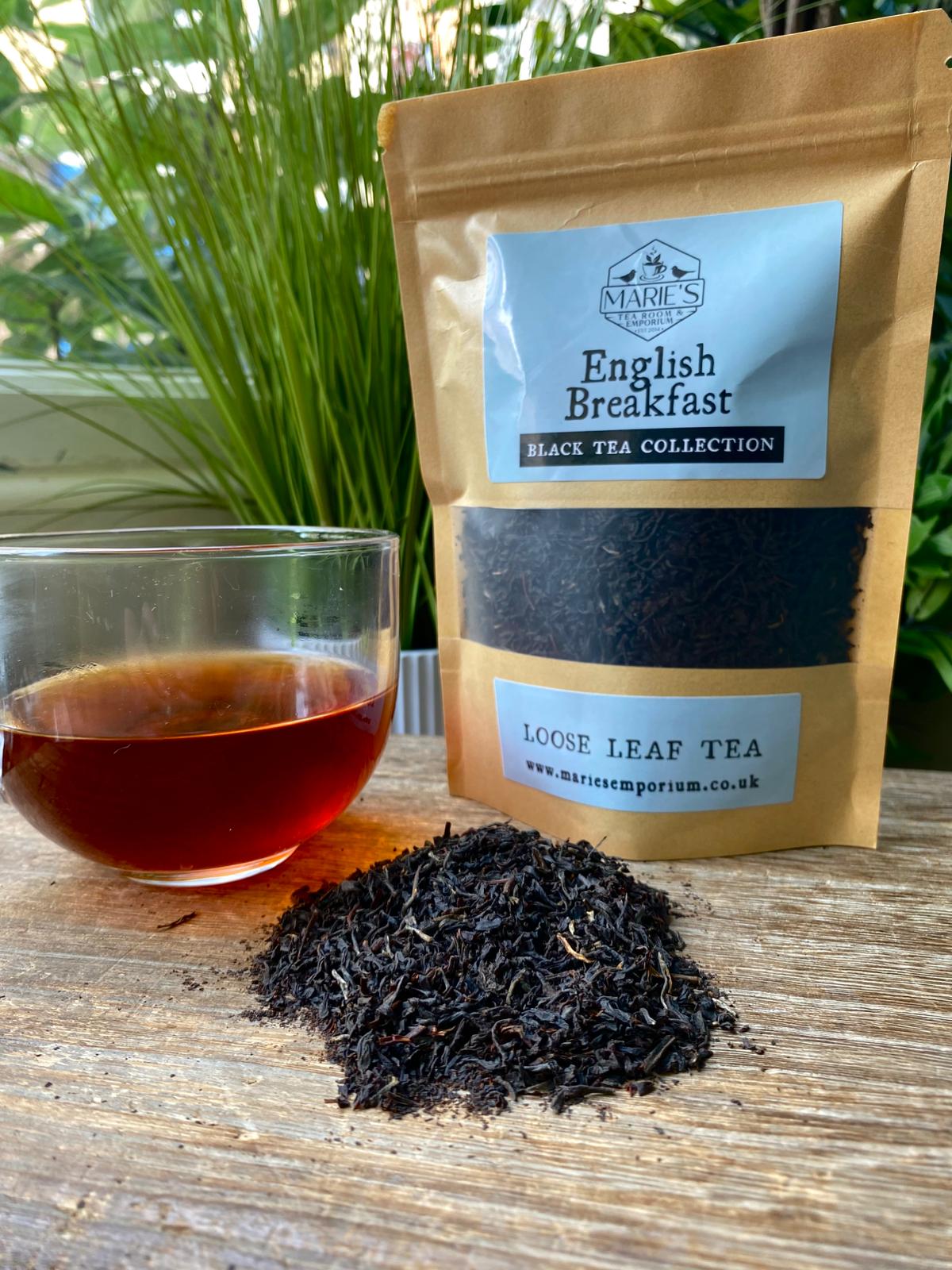 Marie's Emporium English Breakfast loose leaf tea package with a glass of tea and tea leaves on a wooden surface.
