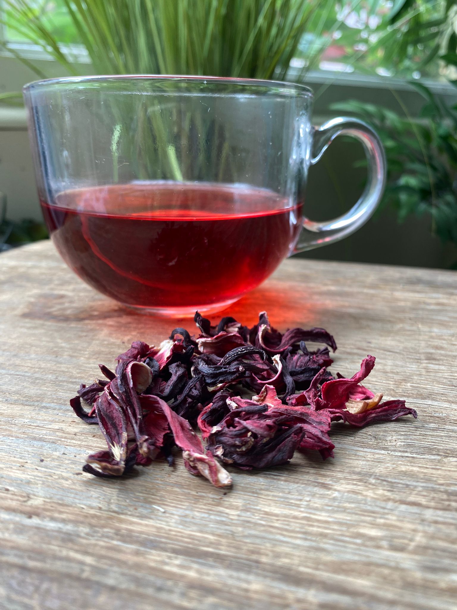 Marie’s hibiscus loose leaf tea with brewed herbal tea in a clear glass mug and loose tea leaves on a wooden surface