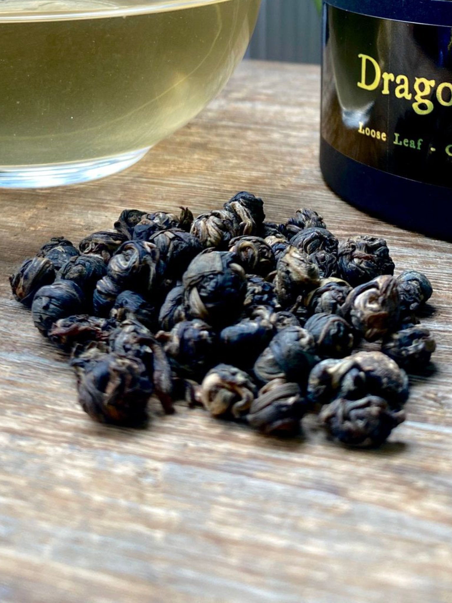 Jasmine dragon peals loose leaf tea leaves on a wooden surface with greenery in the background