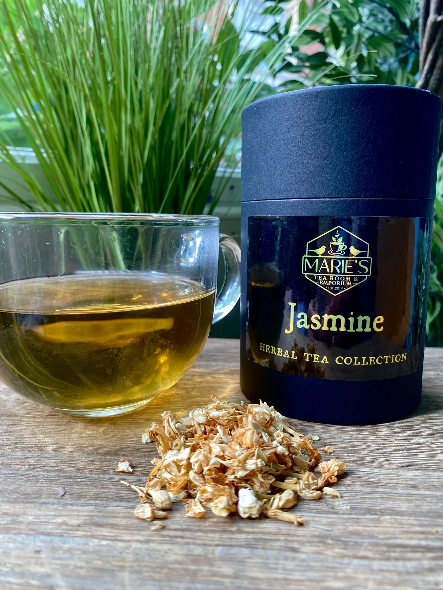 Marie's Tea Jasmine herbal tea canister with a cup of tea and dried tea leaves on a wooden surface.