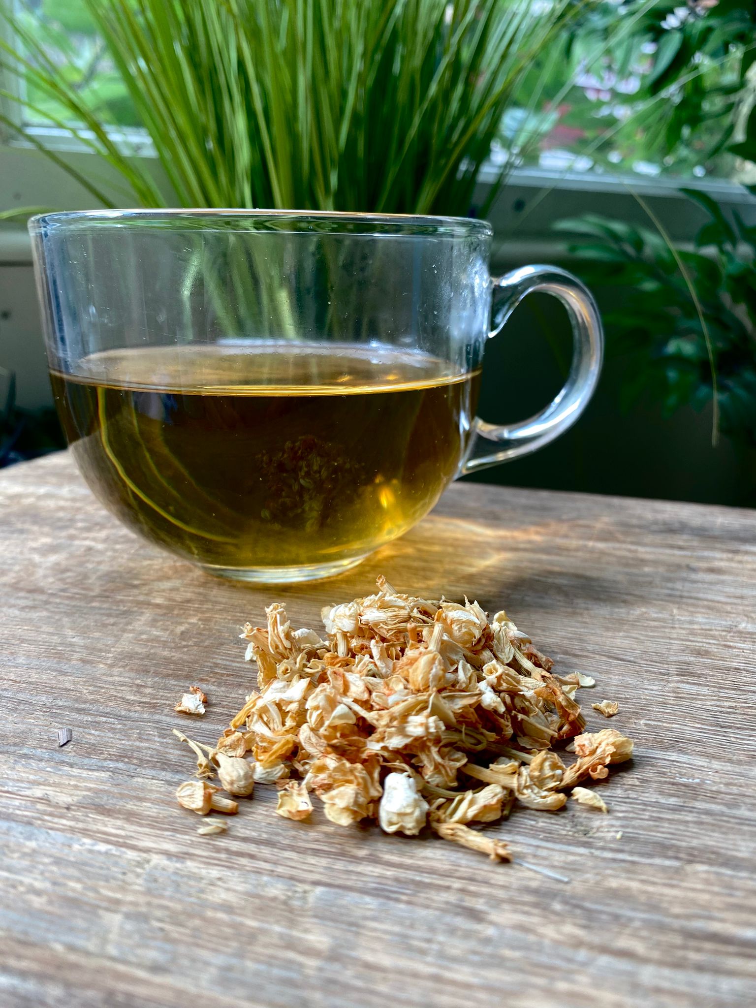 Marie’s Jasmine loose leaf tea with brewed herbal tea in a clear glass mug and loose tea leaves on a wooden surface