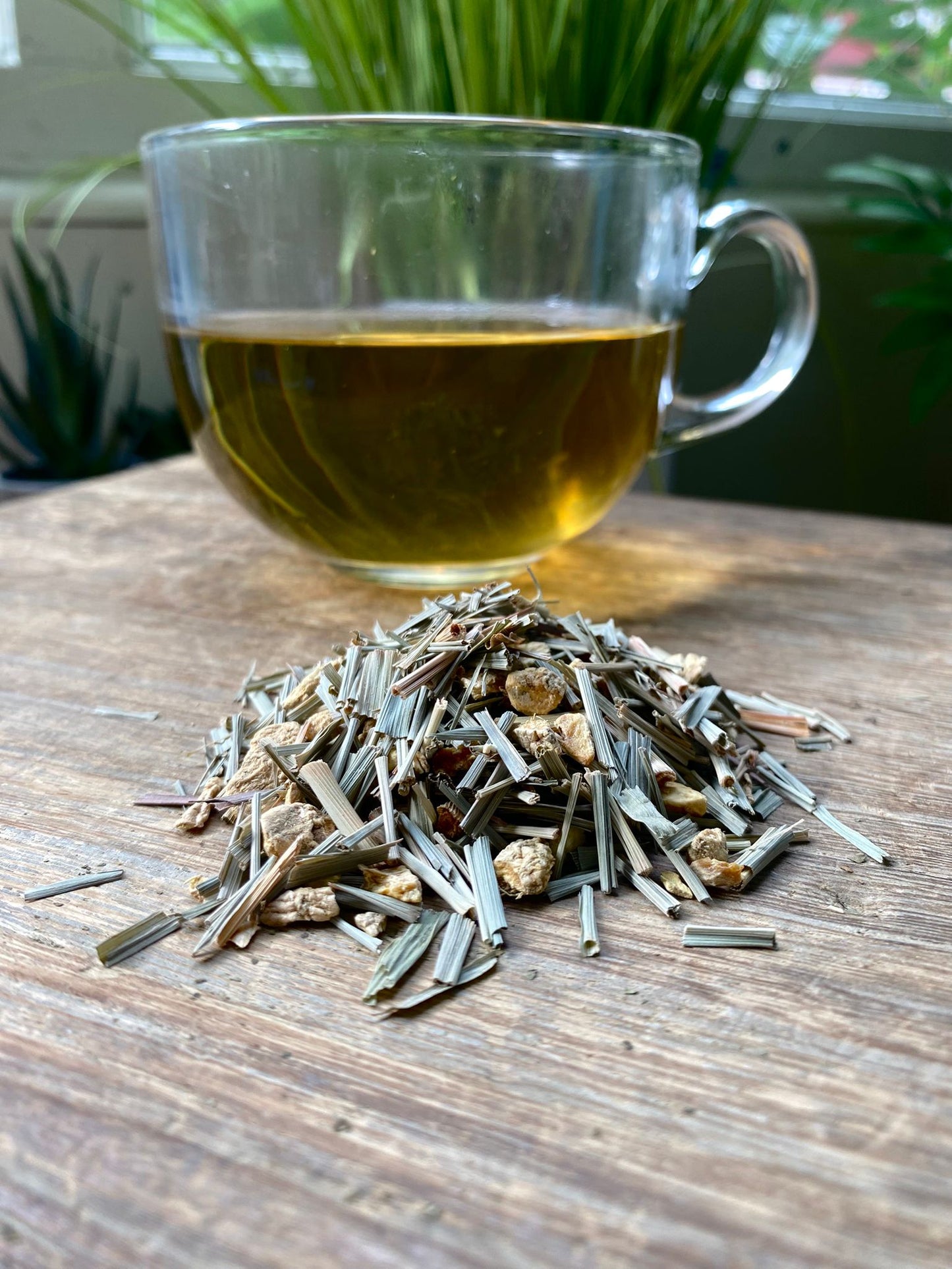 Maries Lemon and Ginger tea leaves and a glass of tea on a wooden surface with plants in the background