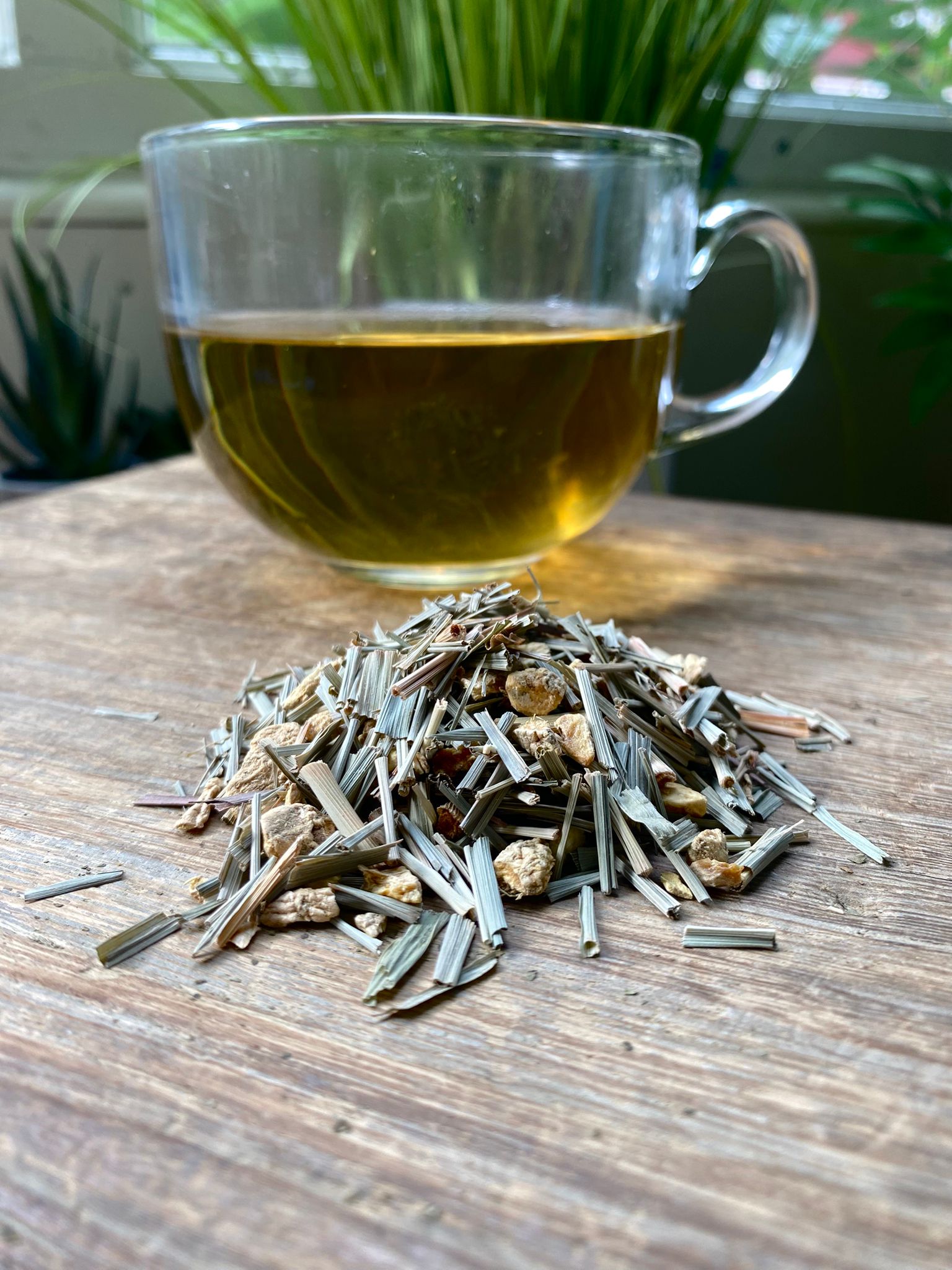 Maries Lemon and Ginger tea leaves and a glass of tea on a wooden surface with plants in the background