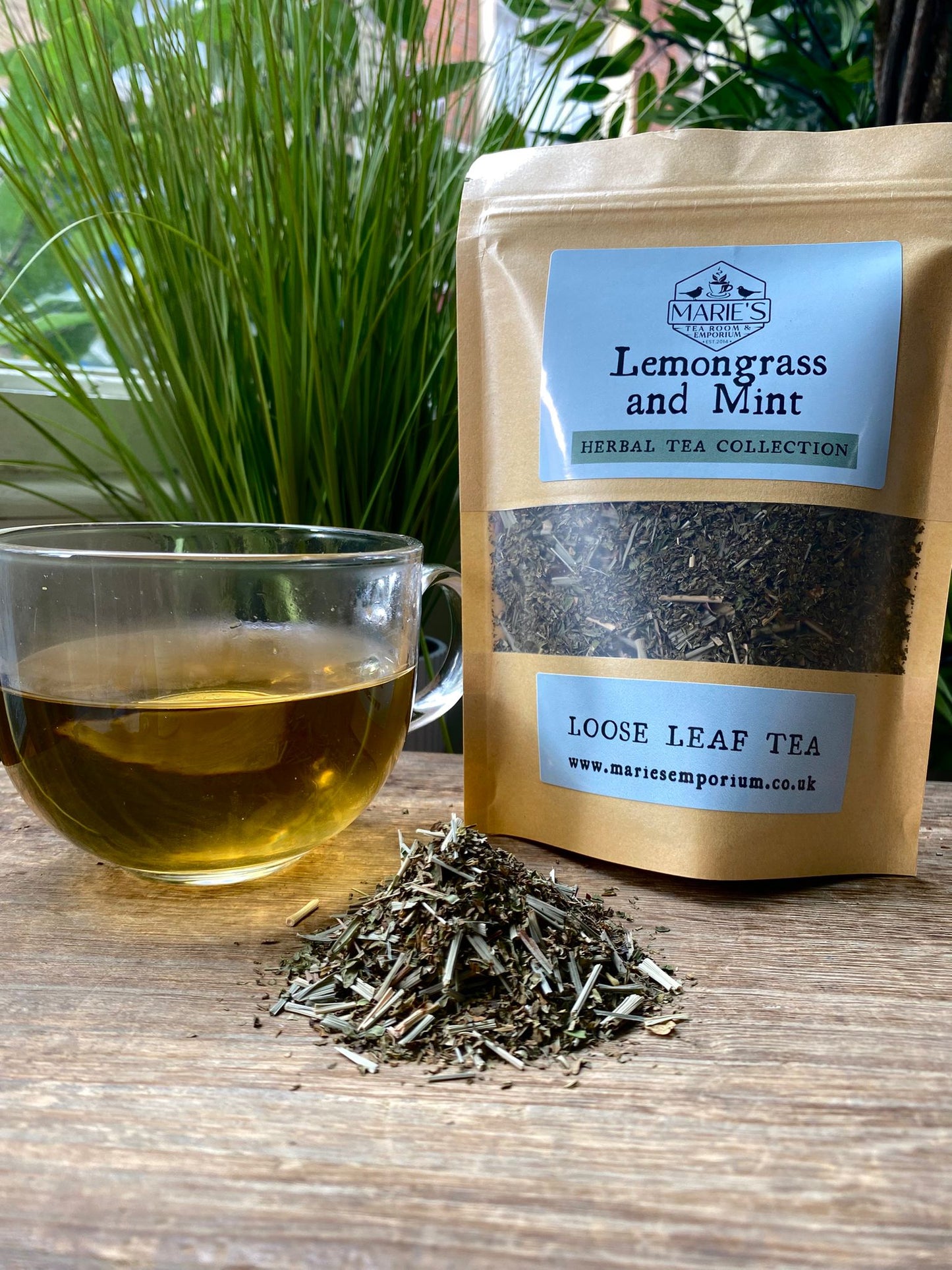 maries lemongrass and mint tea packaging with a glass of tea and loose tea leaves on a wooden surface.