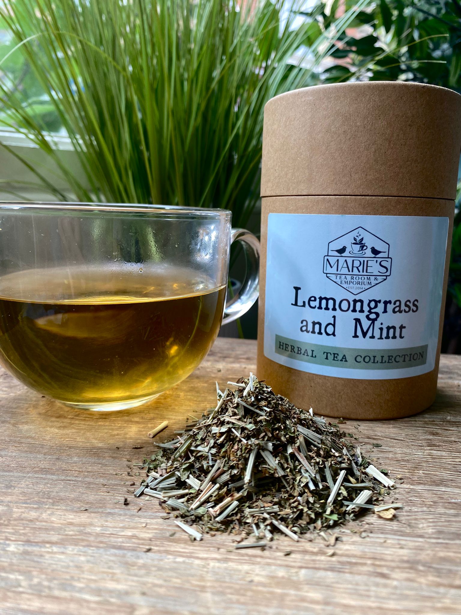 Marie's Lemongrass and Mint tea packaging with a cup of tea and dried herbs on a wooden surface