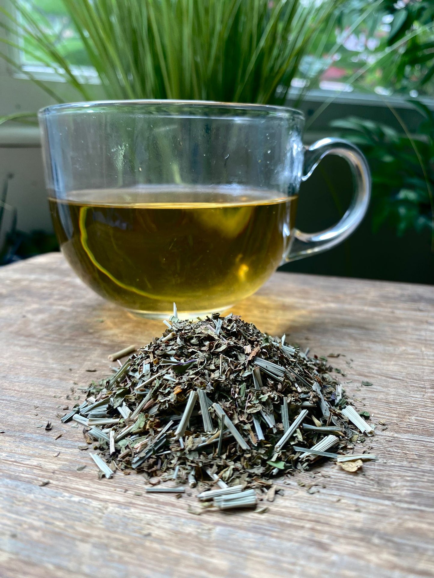 Marie’s lemongrass and mint loose leaf tea with brewed herbal tea in a clear glass mug and loose tea leaves on a wooden surface