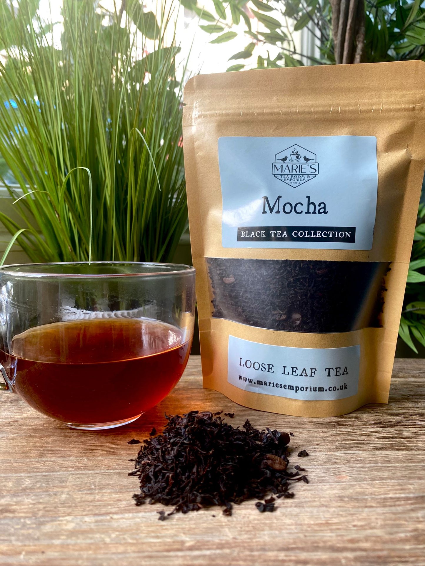 Maries brand Mocha black tea package with a glass of tea and loose tea leaves on a wooden surface.