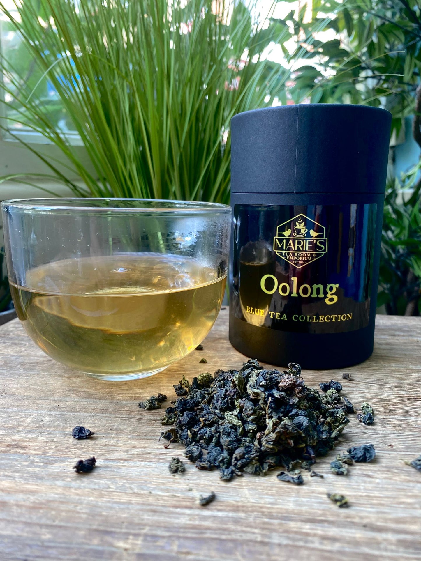 Marie's Oolong tea canister with a glass of tea and loose tea leaves on a wooden surface.