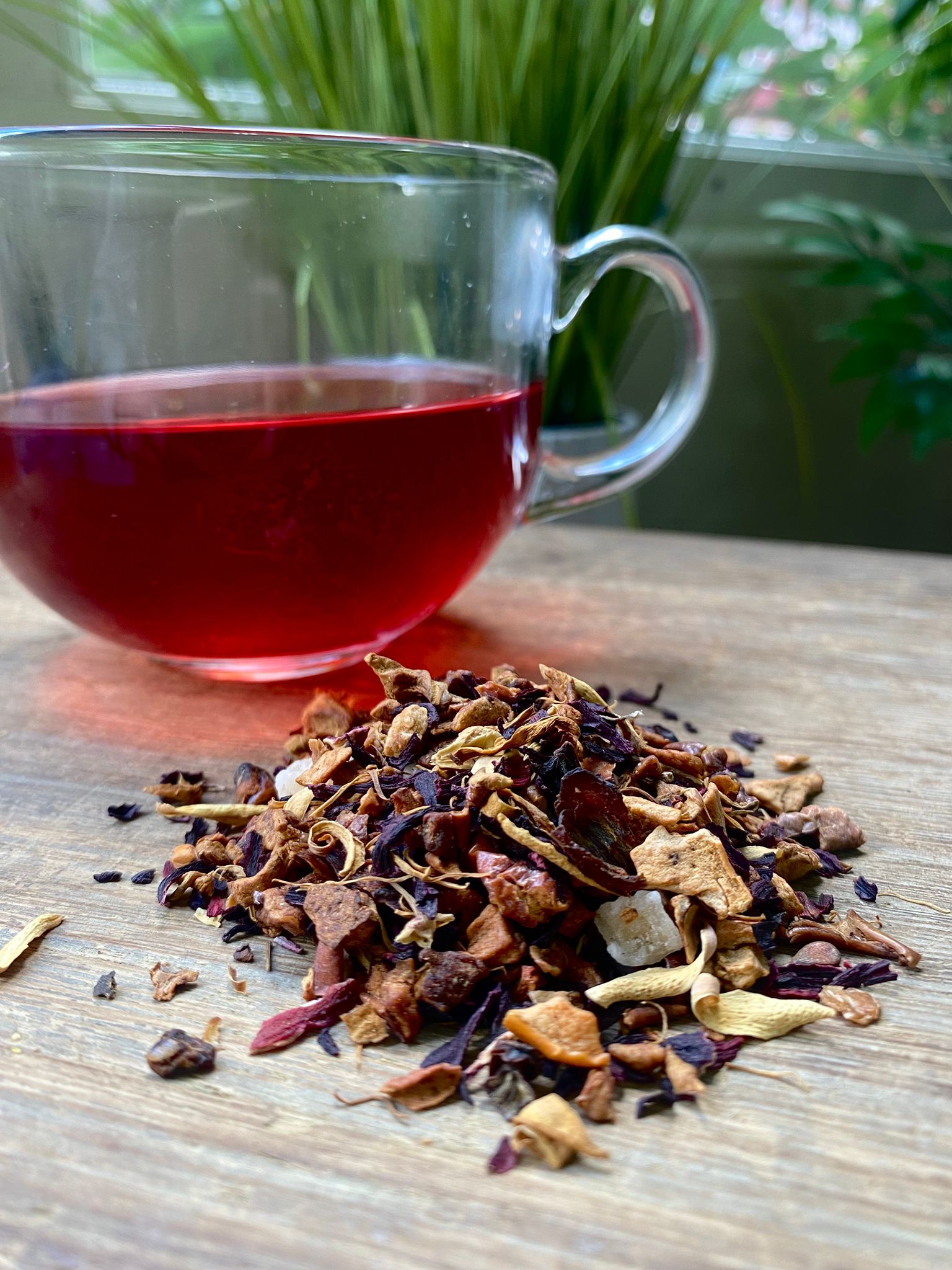 Marie’s Orange and Passionfruit loose leaf tea with brewed red fruit tea in a clear glass mug and loose tea leaves on a wooden surface