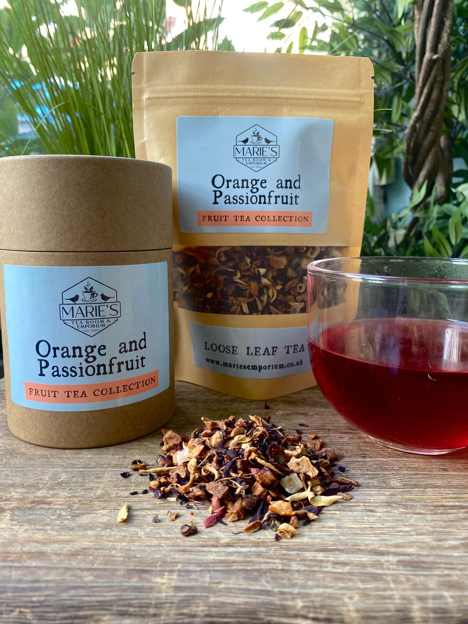 Marie's Orange and Passionfruit tea set with loose tea, packaging, and a cup of tea on a wooden surface.