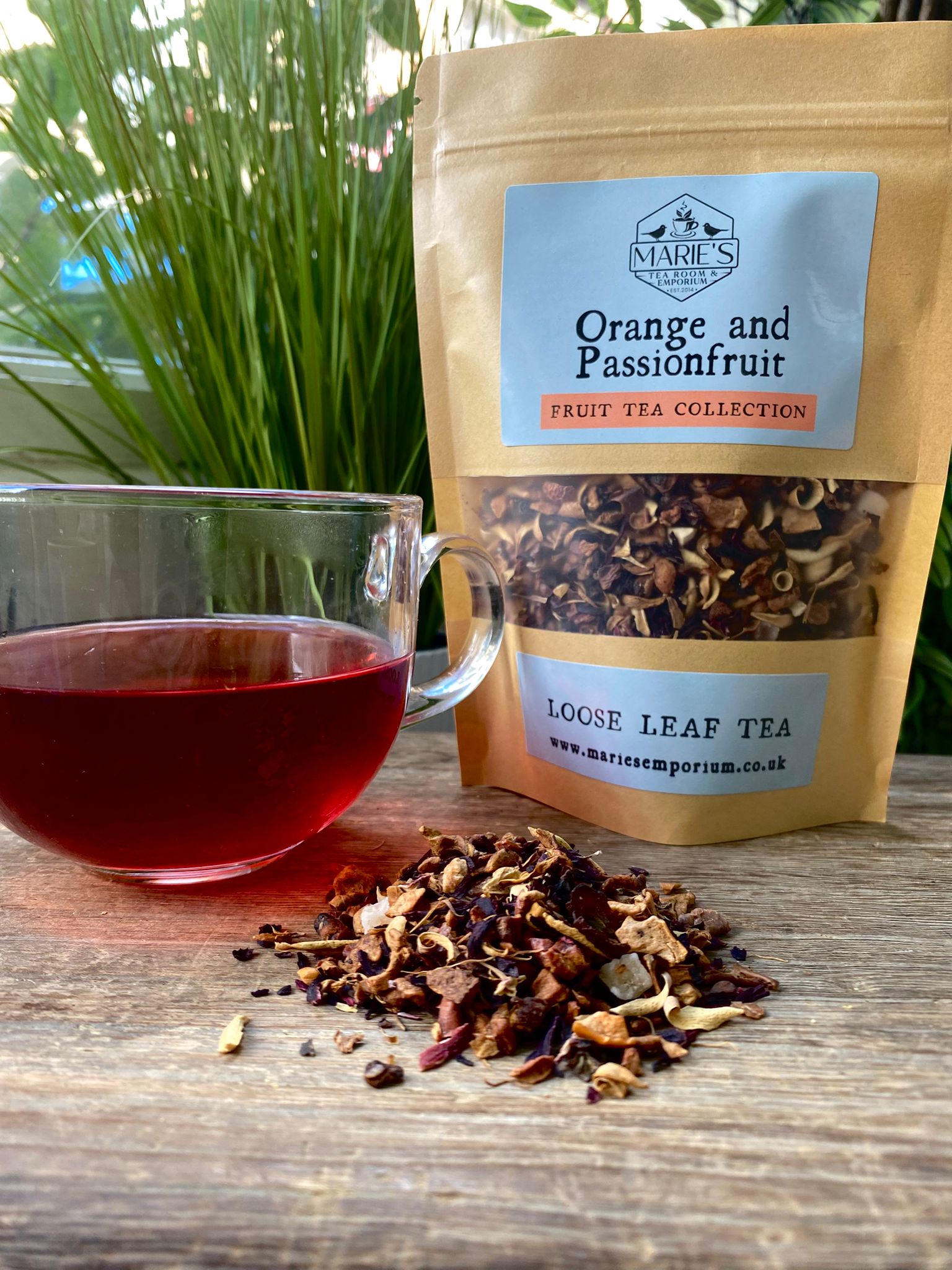 Maries Orange and Passionfruit loose leaf tea package with a glass of tea on a wooden surface.