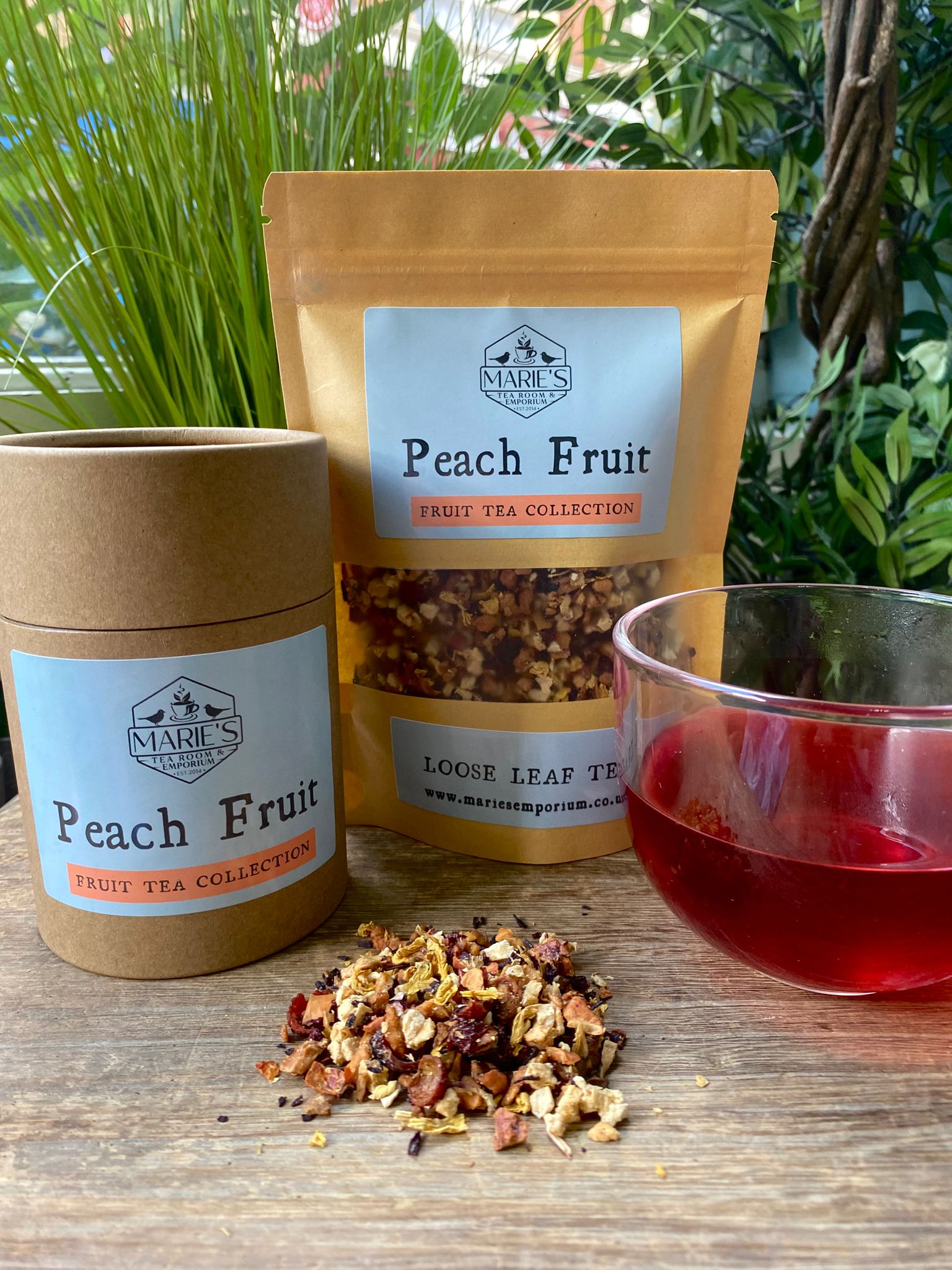 Marle's Peach Fruit tea set with packaging, loose tea, and a glass of tea on a wooden surface.