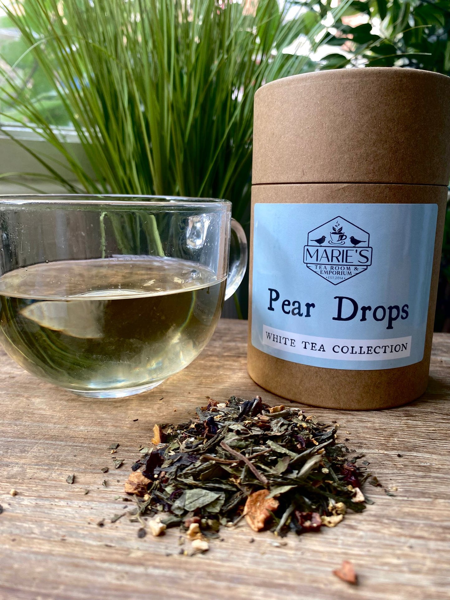 Tea packaging labeled 'Pear Drops' from Marie's Teas with a glass of tea and tea leaves on a wooden surface.