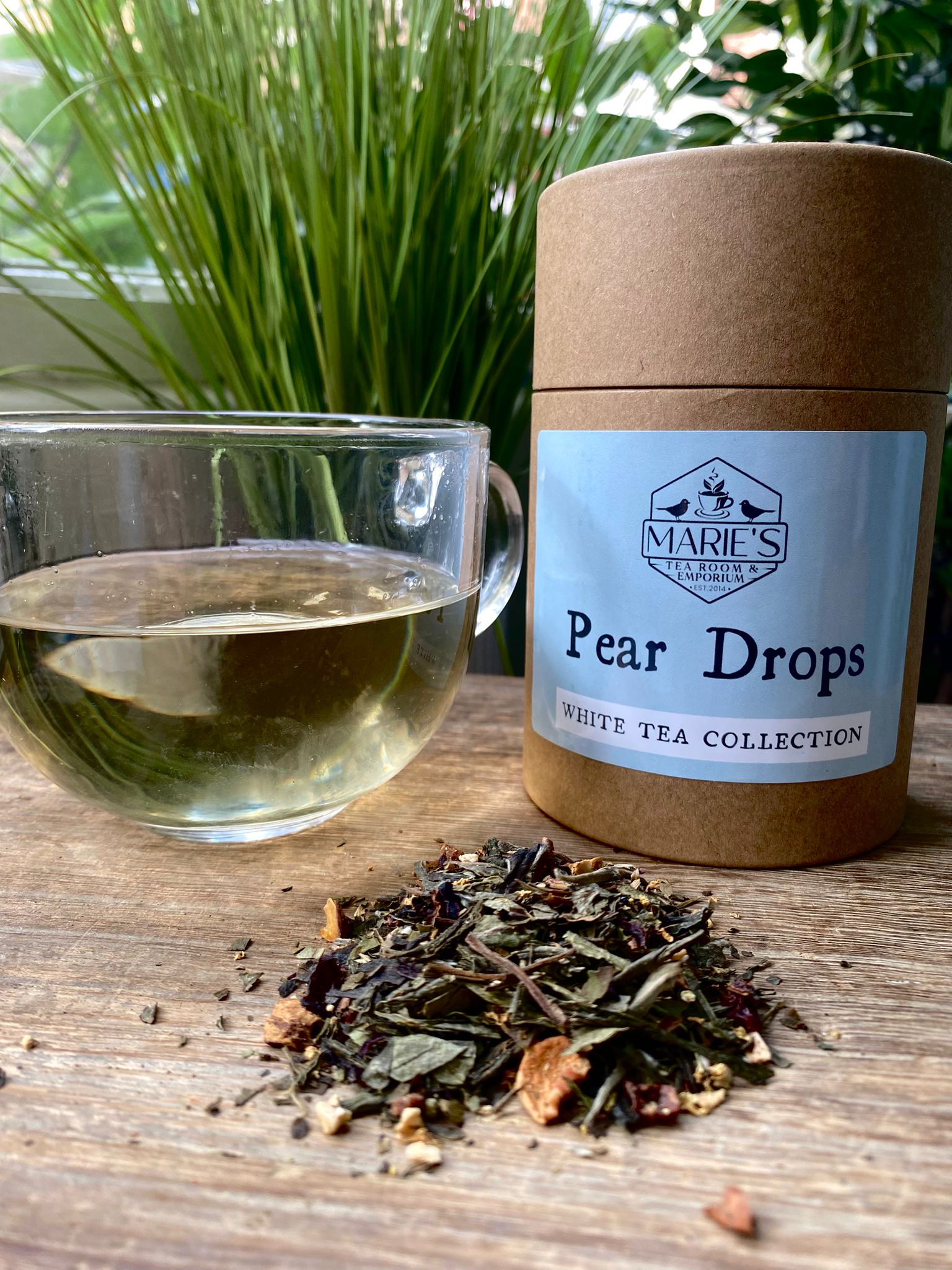 Tea packaging labeled 'Pear Drops' from Marie's Teas with a glass of tea and tea leaves on a wooden surface.