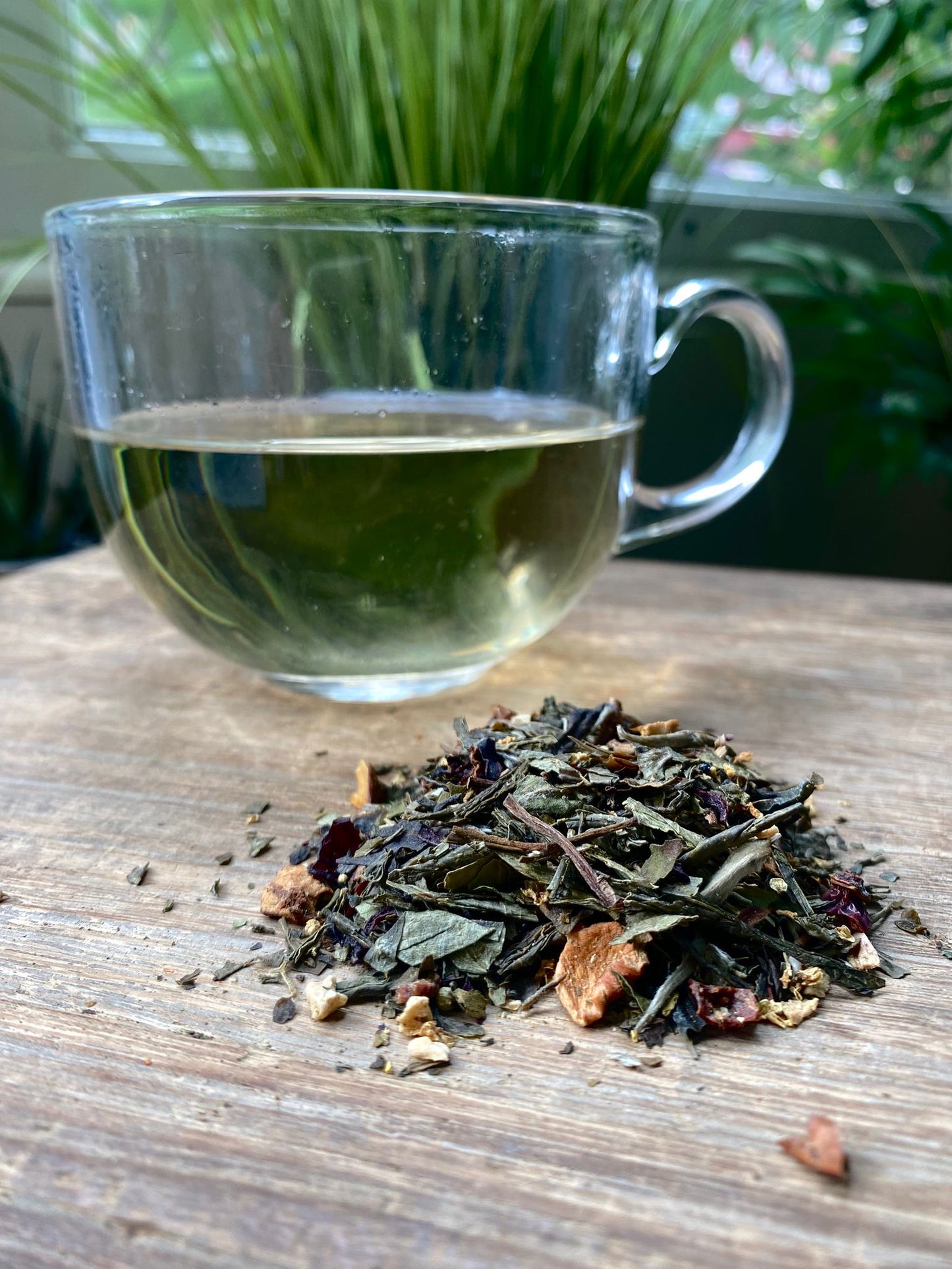 Clear glass mug with pear drops white tea and a pile of dried tea leaves on a wooden surface.