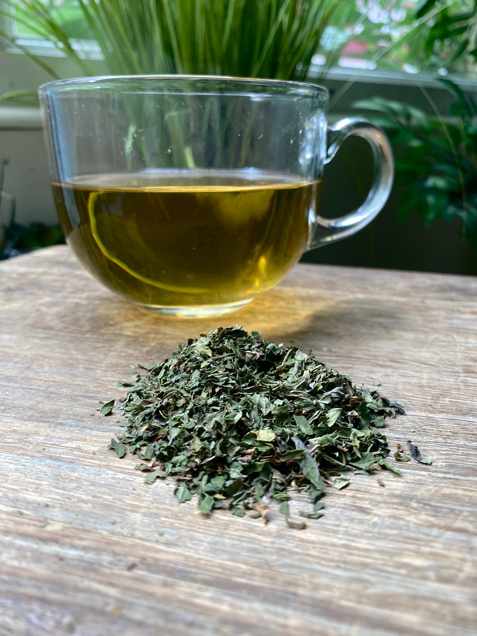 Marie’s peppermint loose leaf tea with brewed herbal tea in a clear glass mug and loose tea leaves on a wooden surface