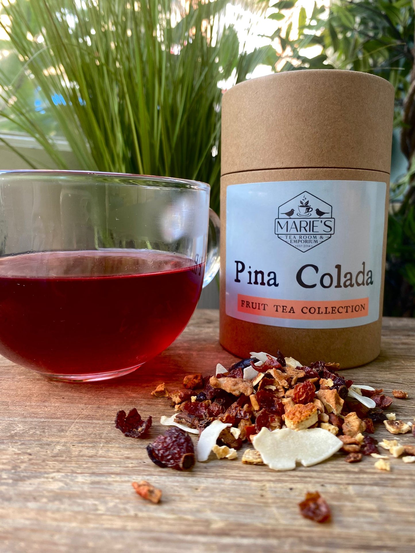 Marie's Pina Colada fruit tea packaging with a glass of tea and tea leaves on a wooden surface.