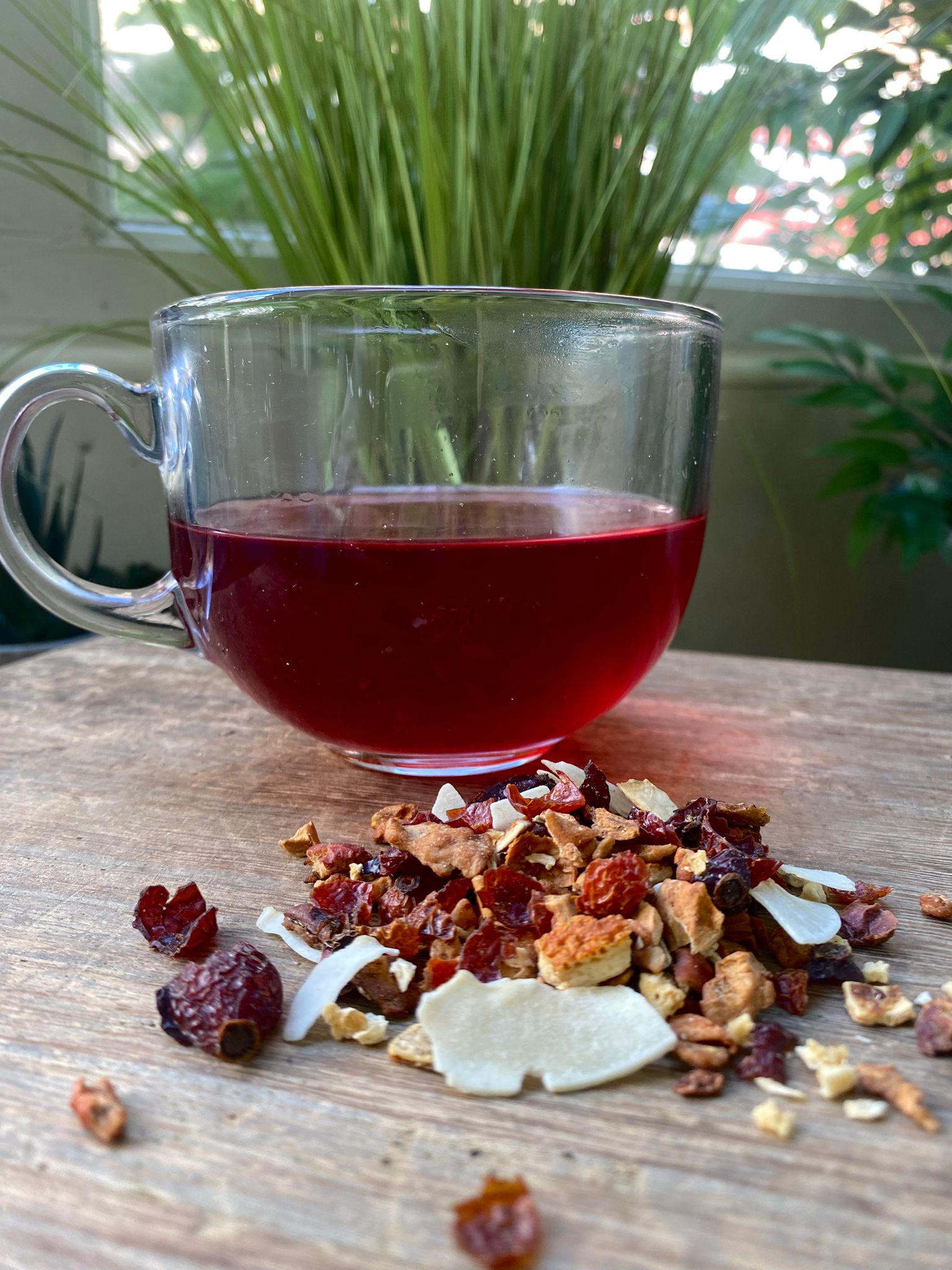 Marie’s Pina Colada loose leaf tea with brewed fruit tea in a clear glass mug and loose tea leaves on a wooden surface