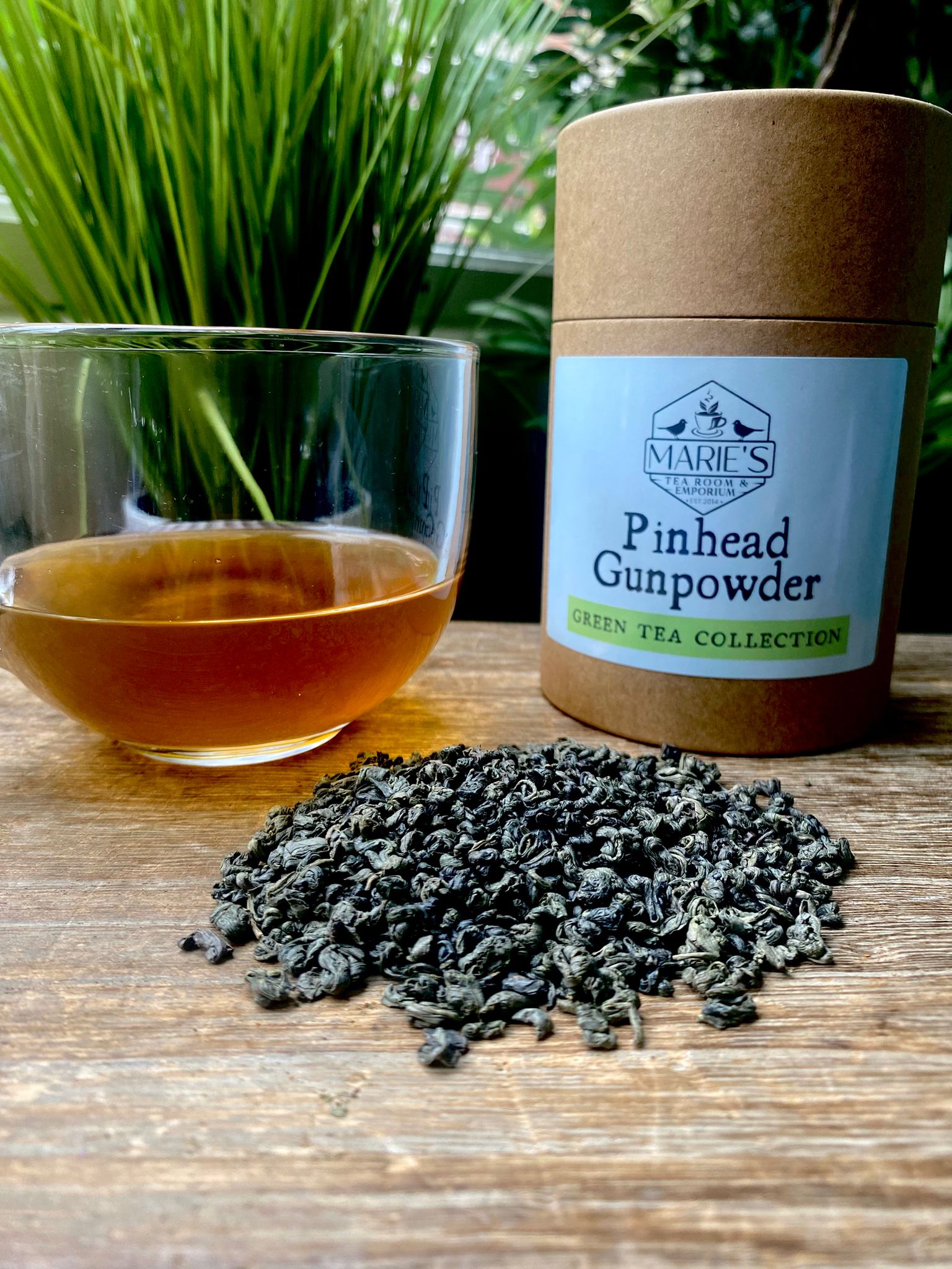 maries Pinhead Gunpowder with tea leaves and a glass of tea on a wooden surface.